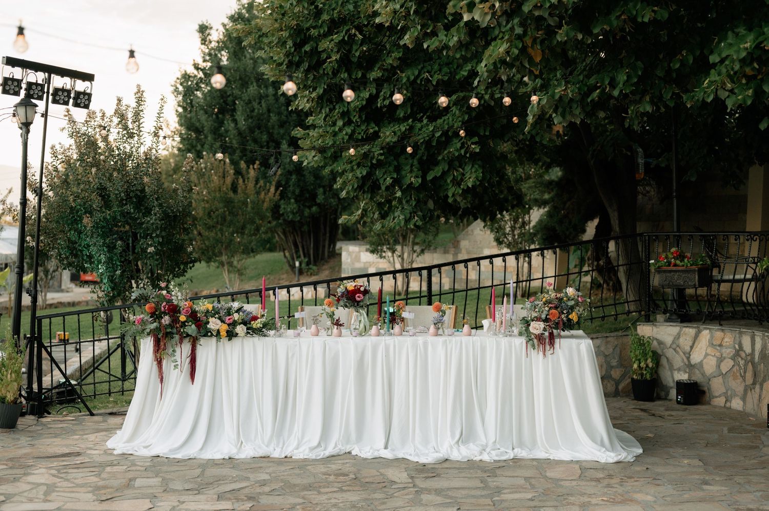 A row of white wedding dresses hanging on display outdoors between trees in a garden setting.
