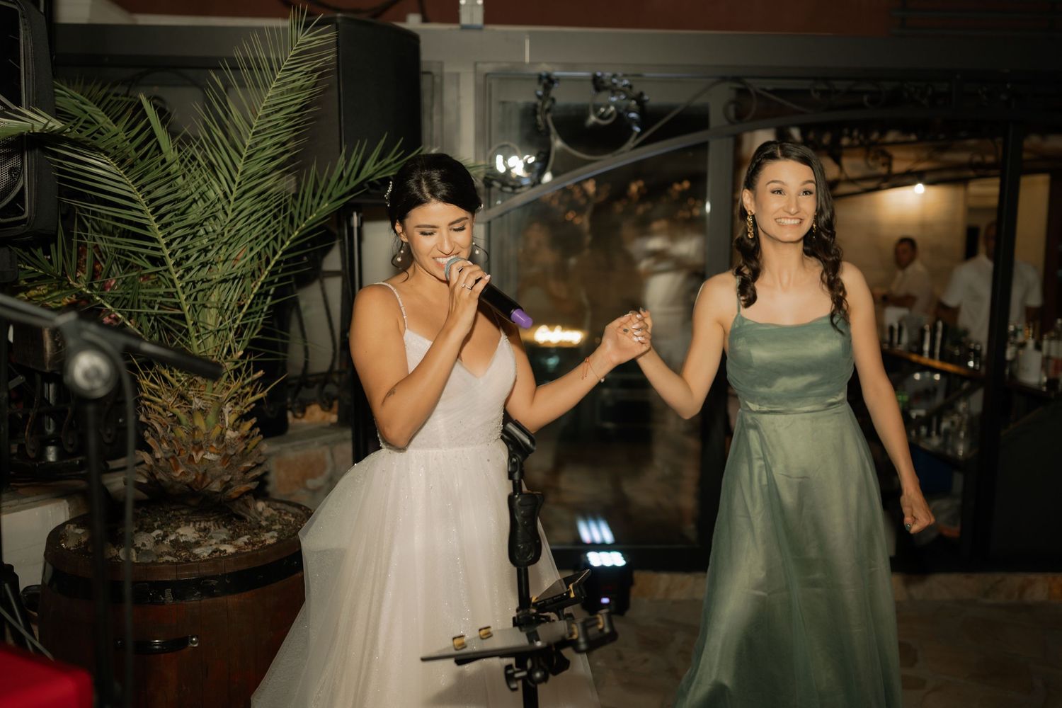 Wedding party members in sage green dresses dance together at an evening reception celebration.