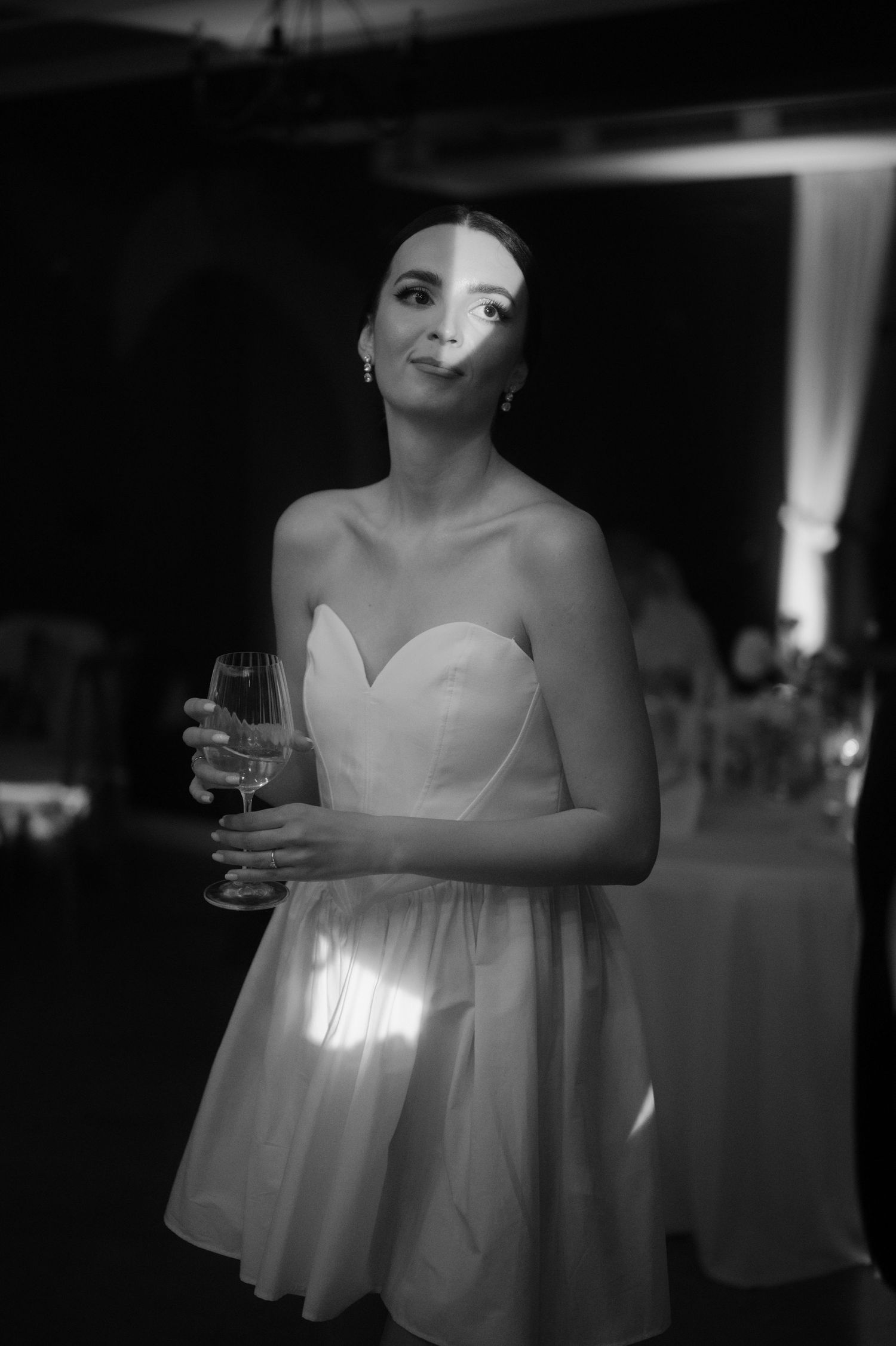 A black and white photo series showing a person in a flowing white dress holding a drink at an elegant event.