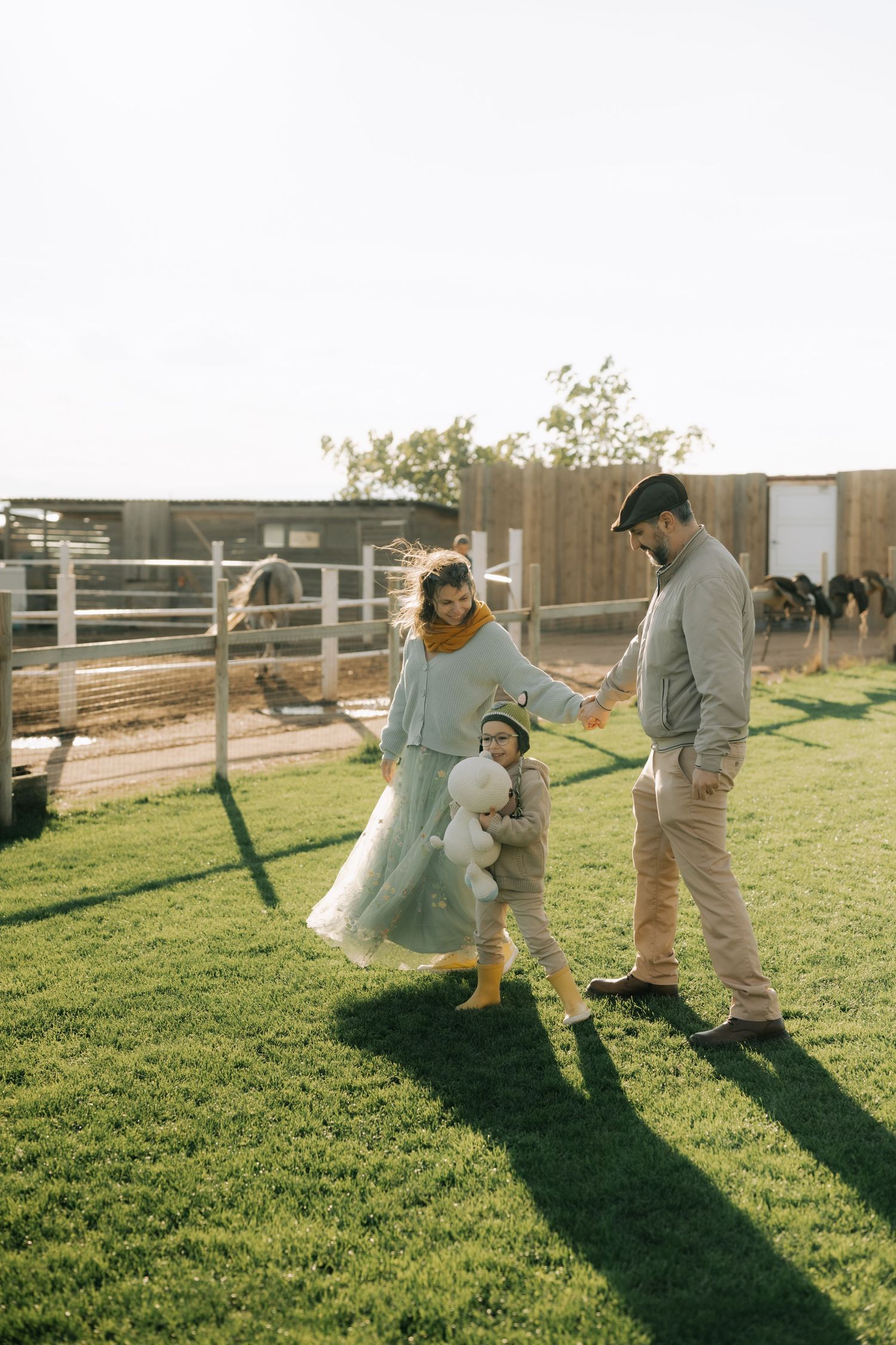 A couple playfully dances together on a sunny lawn with wooden fences in the background casting long shadows.