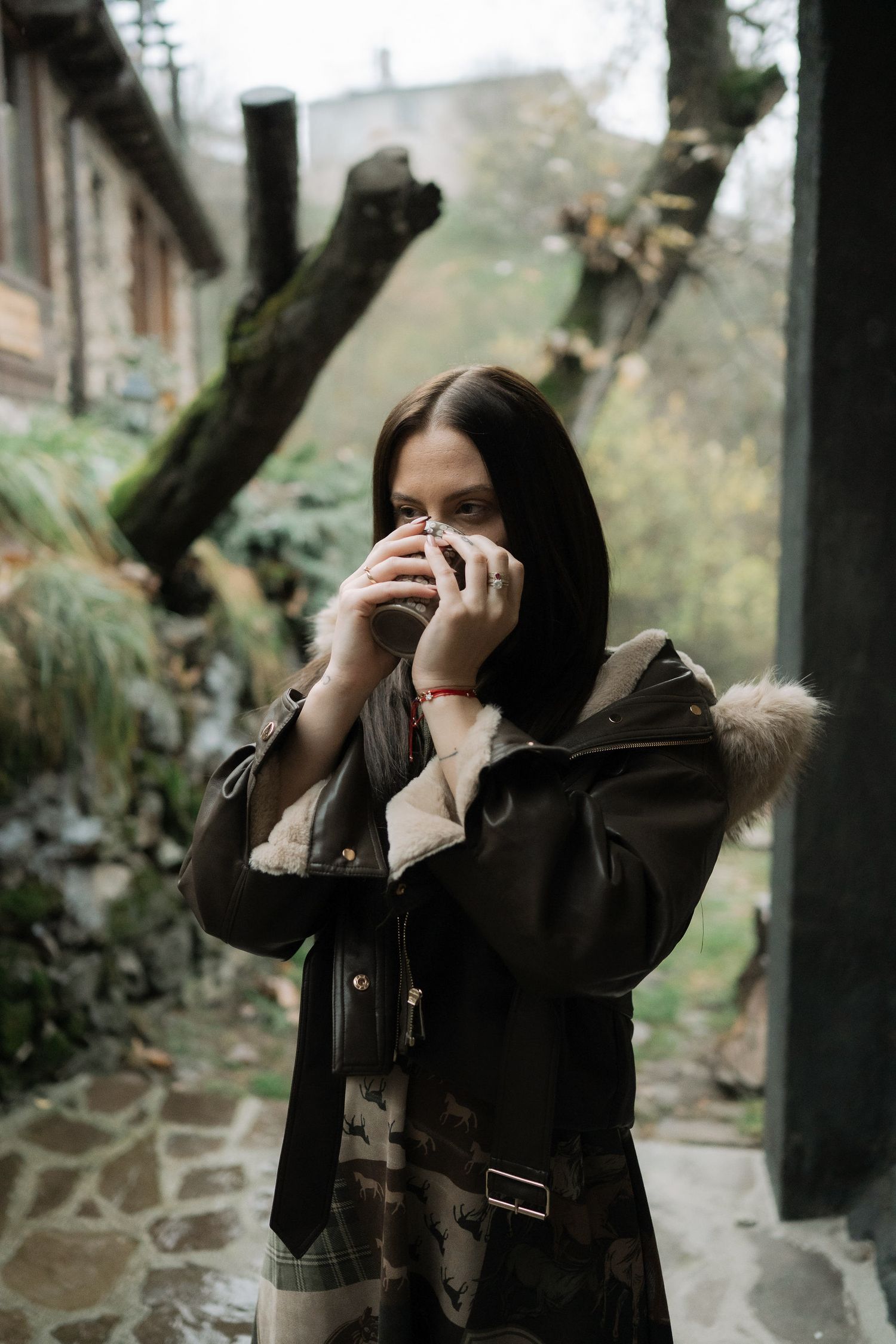 Person in black coat takes photos with a camera in an outdoor setting with trees and branches in the background.