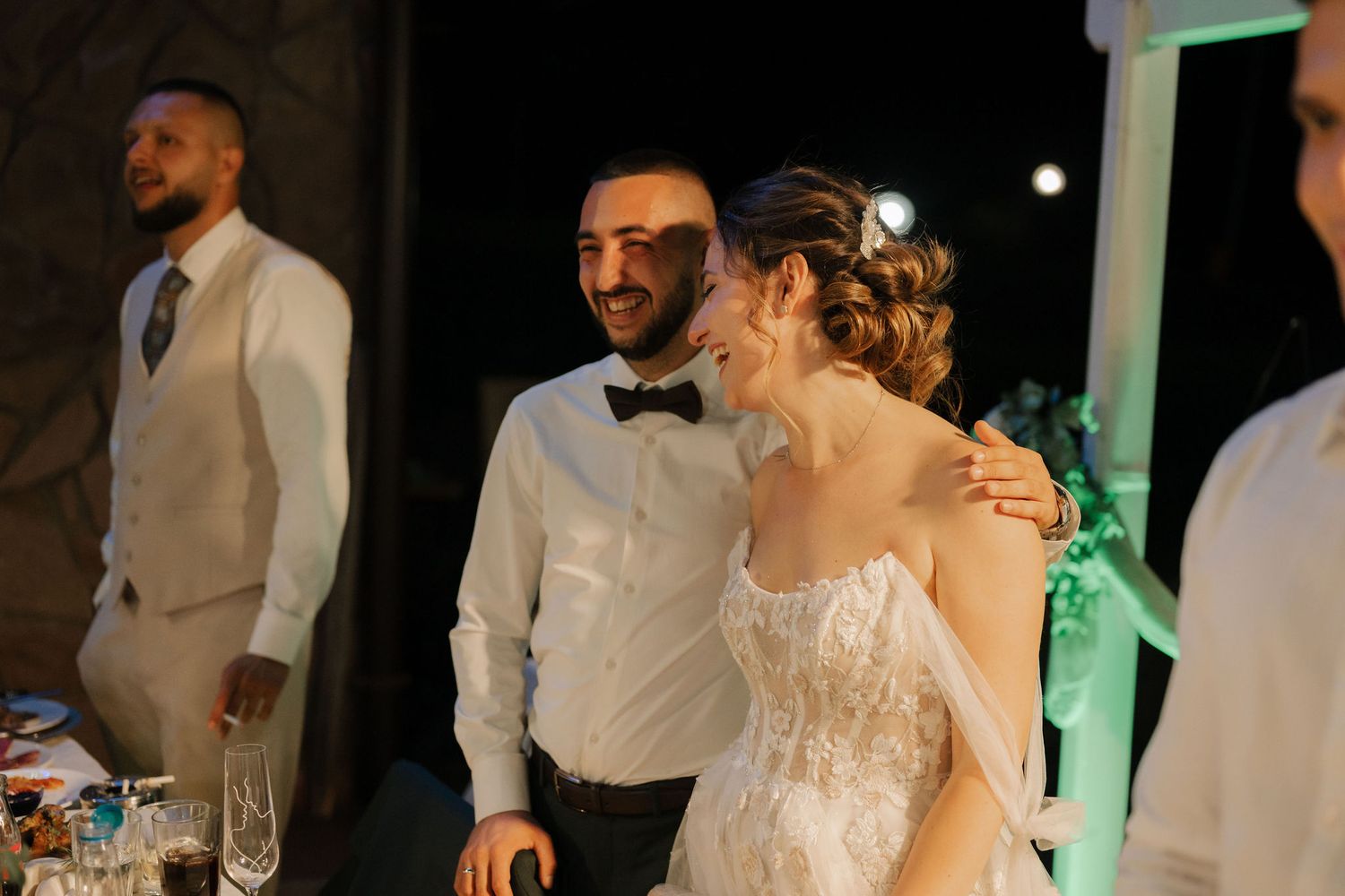 Wedding reception guests dance and celebrate on a dimly lit dance floor with green accent lighting.