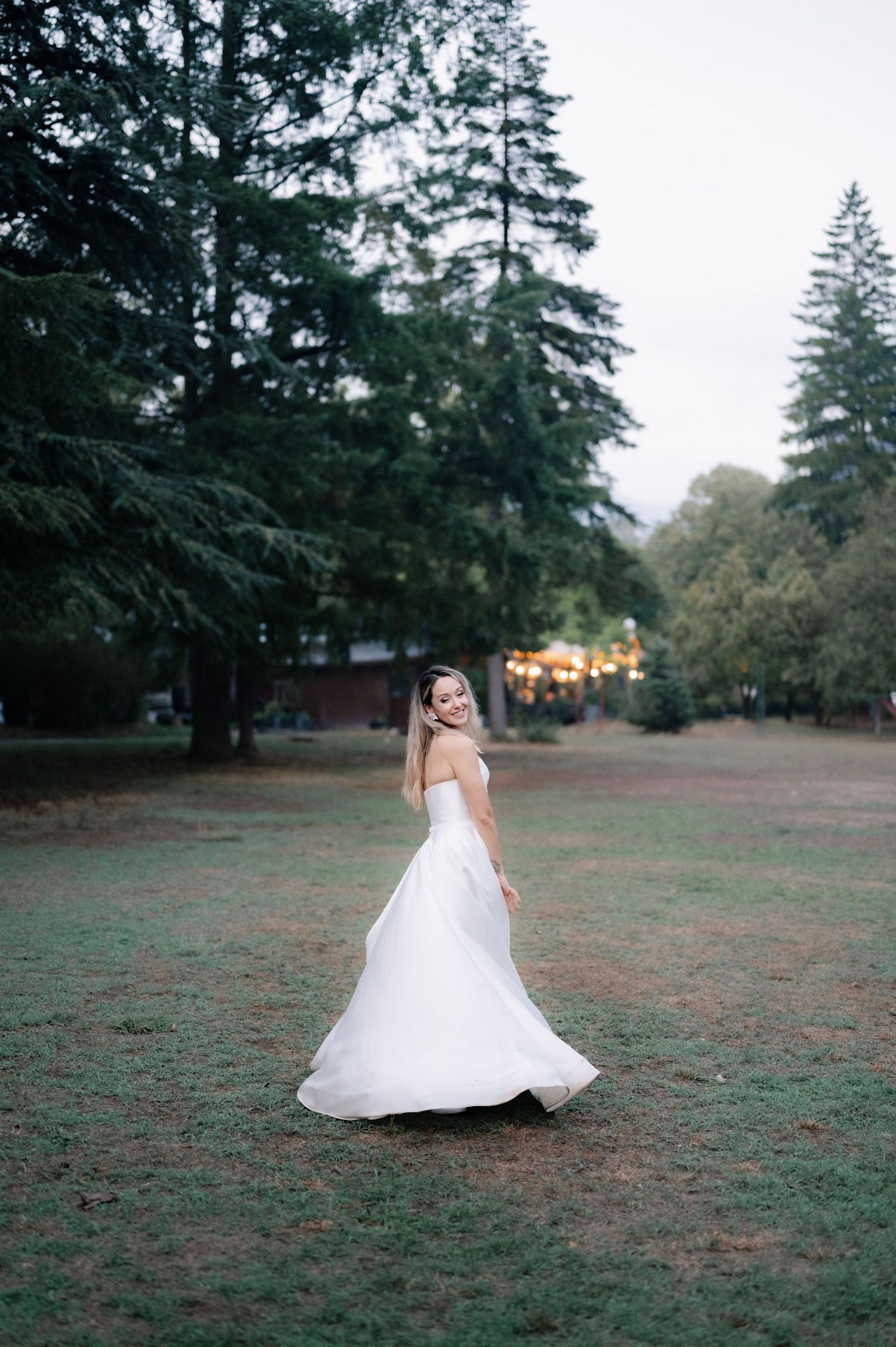 A white wedding dress twirls gracefully in a series of spinning motions across a grassy field at sunset.