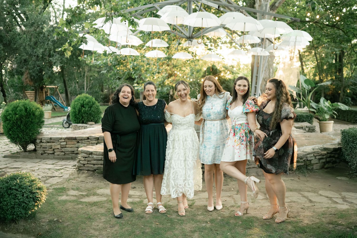 A group of people in formal attire pose together in a lush garden setting during a special outdoor event.