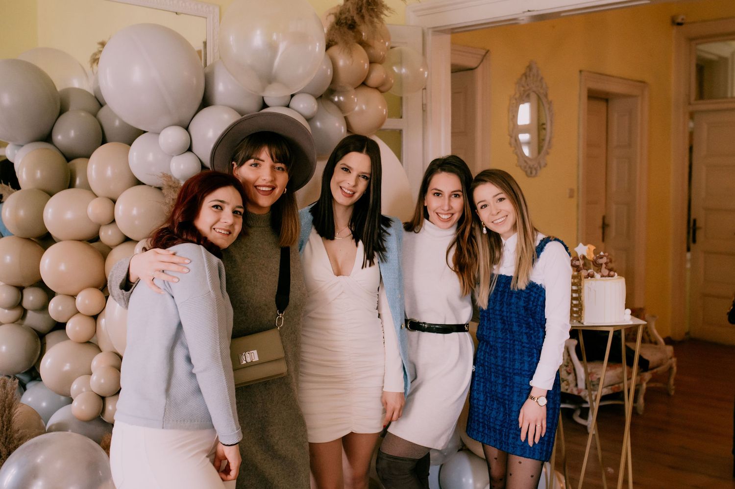 A group of people pose together in a white room decorated with elegant balloon arrangements and white decor.