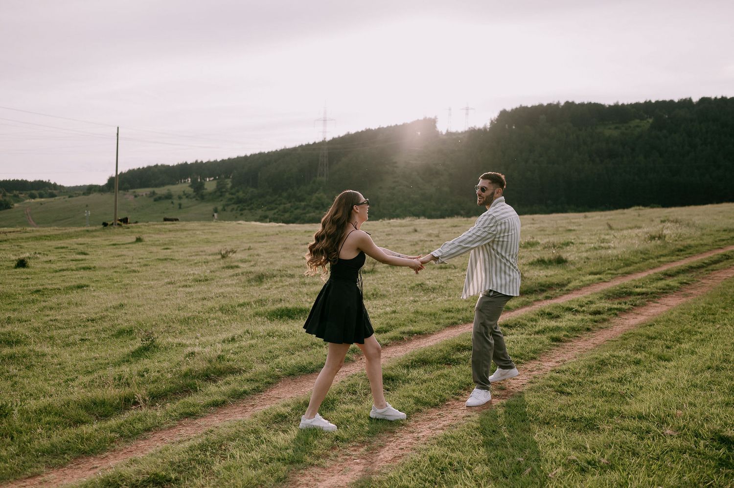 People walking along a scenic dirt path through rolling green hills on a misty afternoon.