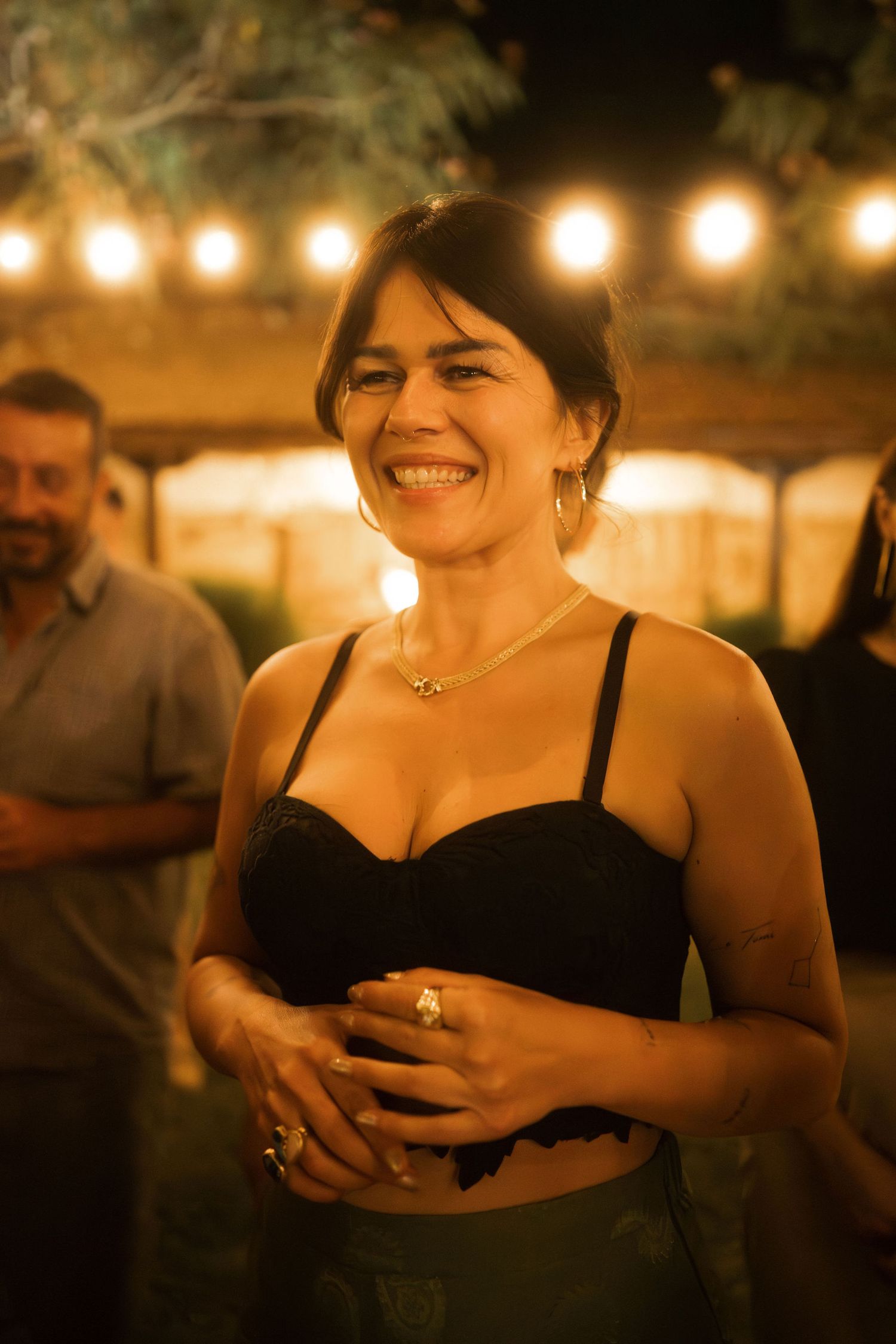 A series of warm-lit candid photos showing someone in a black dress laughing and smiling at an evening event.