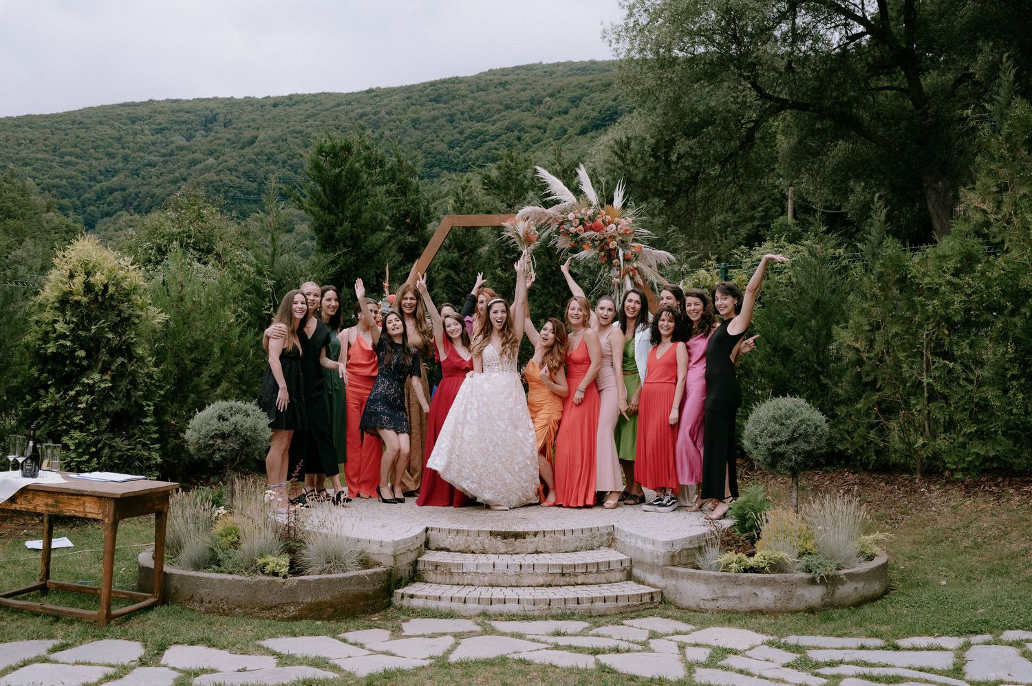 A panoramic collage of an outdoor wedding celebration with guests gathered on a hillside in coordinating red dresses.