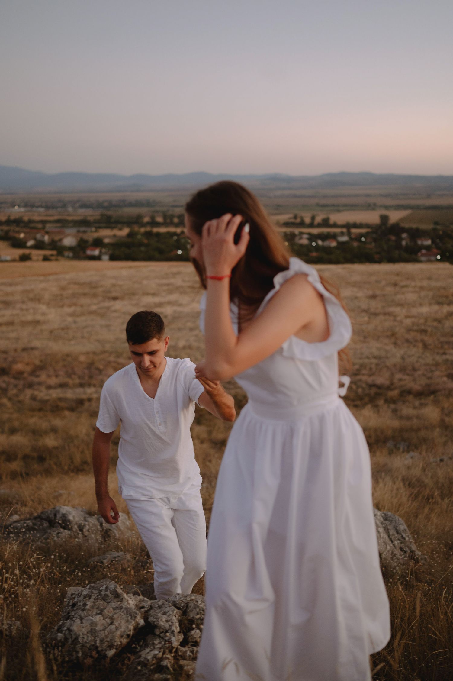 Couple in white outfits share playful moments during sunset photoshoot in a desert landscape.