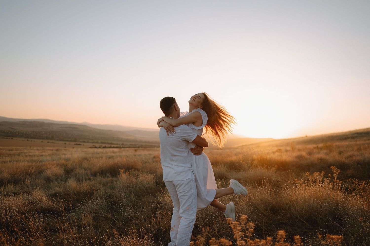 Romantic sunset moment captured in expansive field with warm golden light and rolling hills.