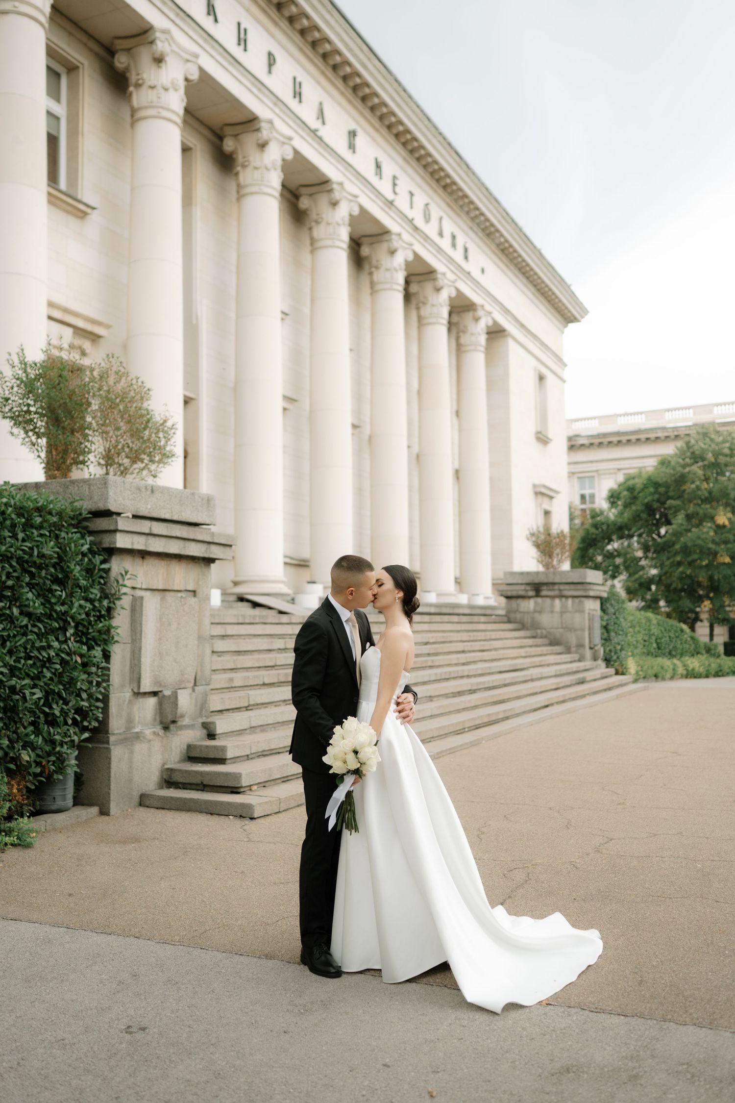 A romantic wedding photo series showing a couple in formal attire against a grand colonnade with white pillars.