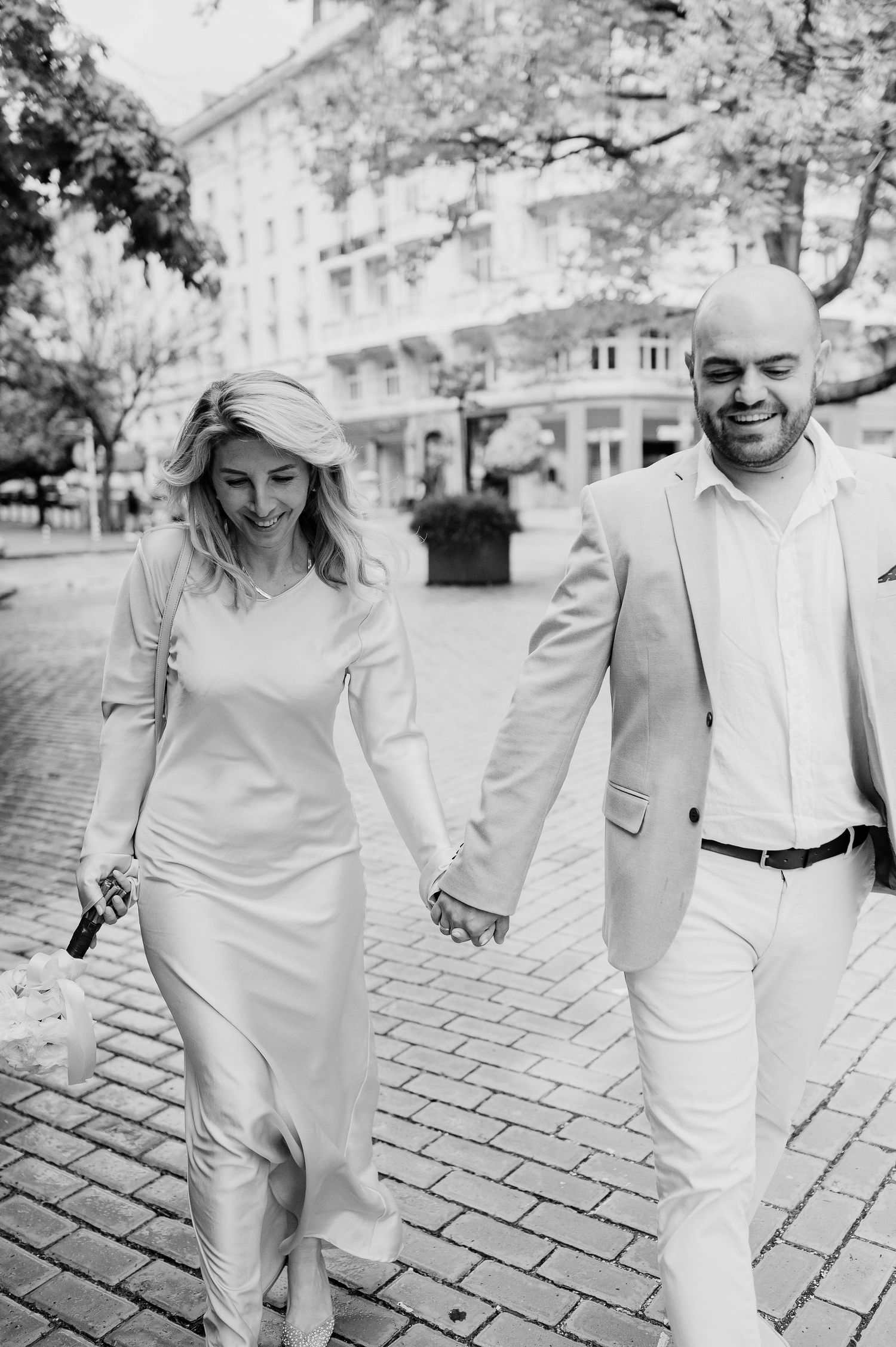 Black and white photo of couple laughing while walking on cobblestone street.