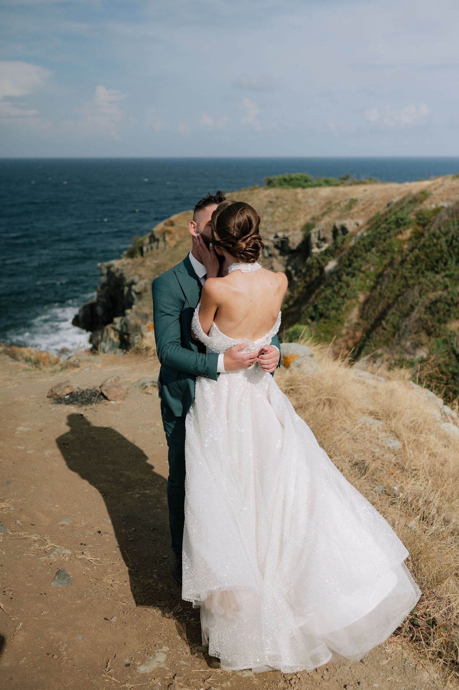 A wedding couple sharing an intimate moment on a scenic coastal cliff.