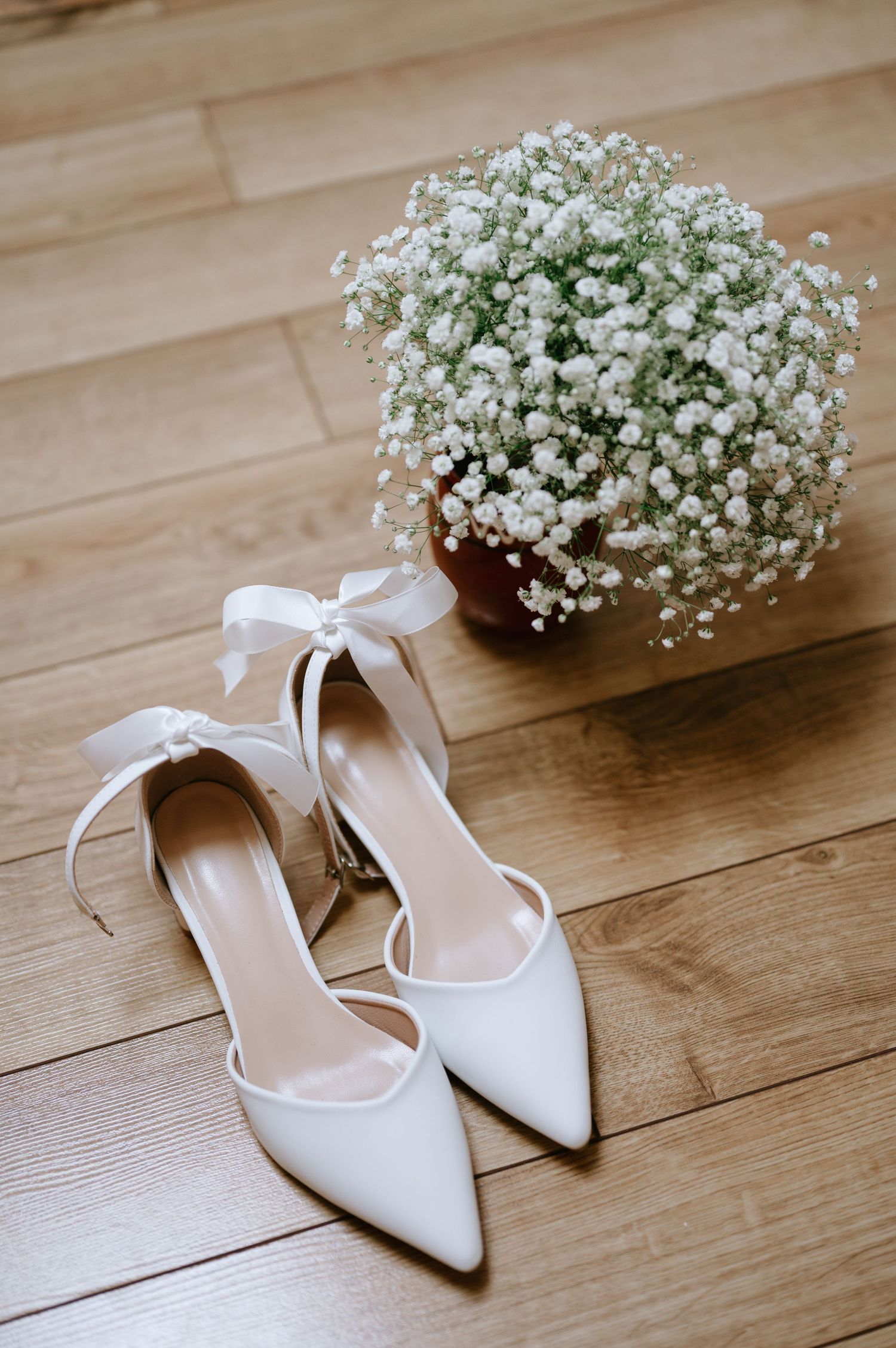 Bridal shoes and baby's breath arrangement styled on hardwood flooring.