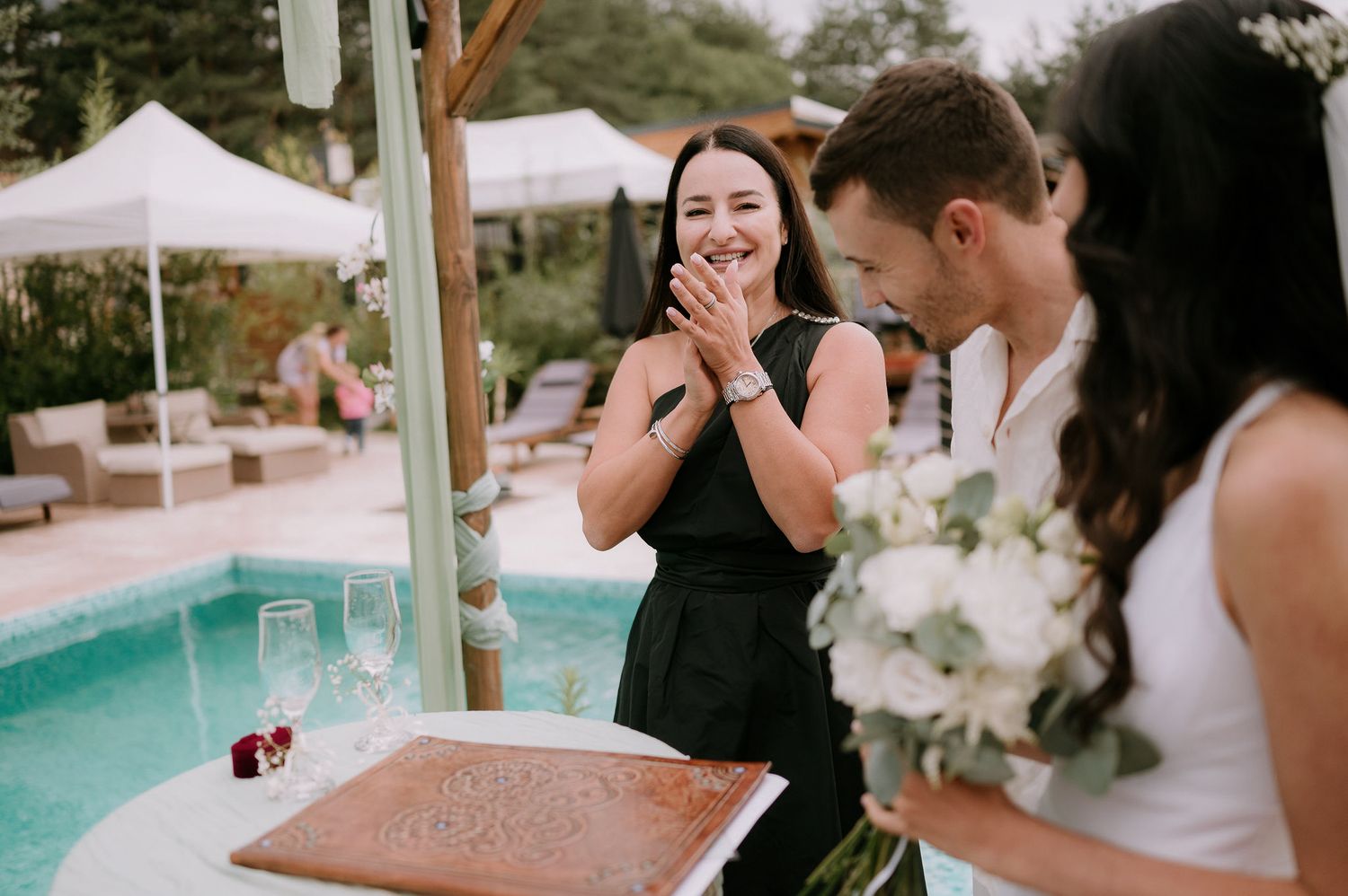 Wedding celebration by turquoise pool with white tent and floral arrangements.
