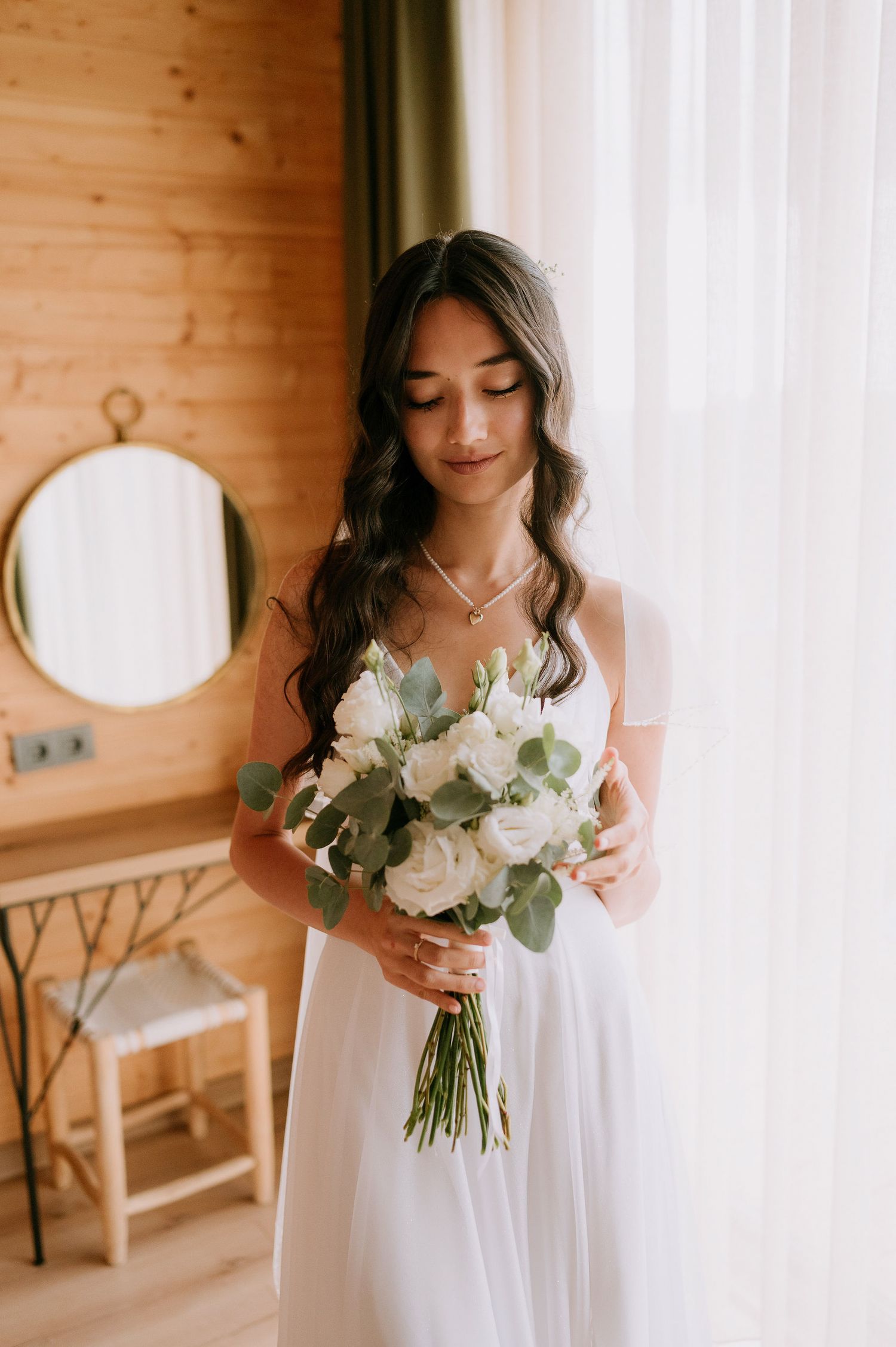 Dreamy bridal portrait with white rose bouquet and flowing dress in sunlit room.