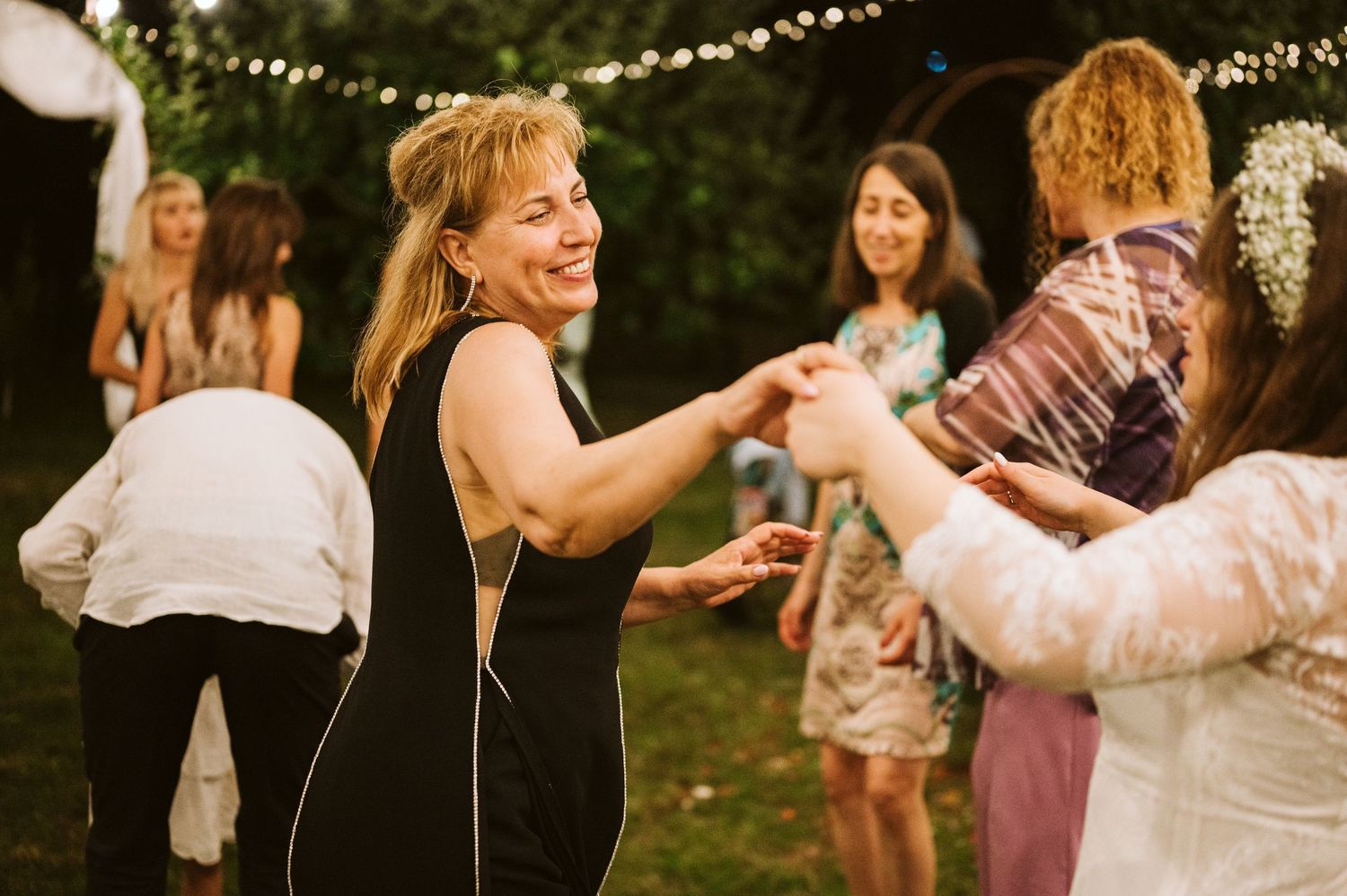 Dancing guests celebrate at an outdoor wedding reception with string lights overhead.