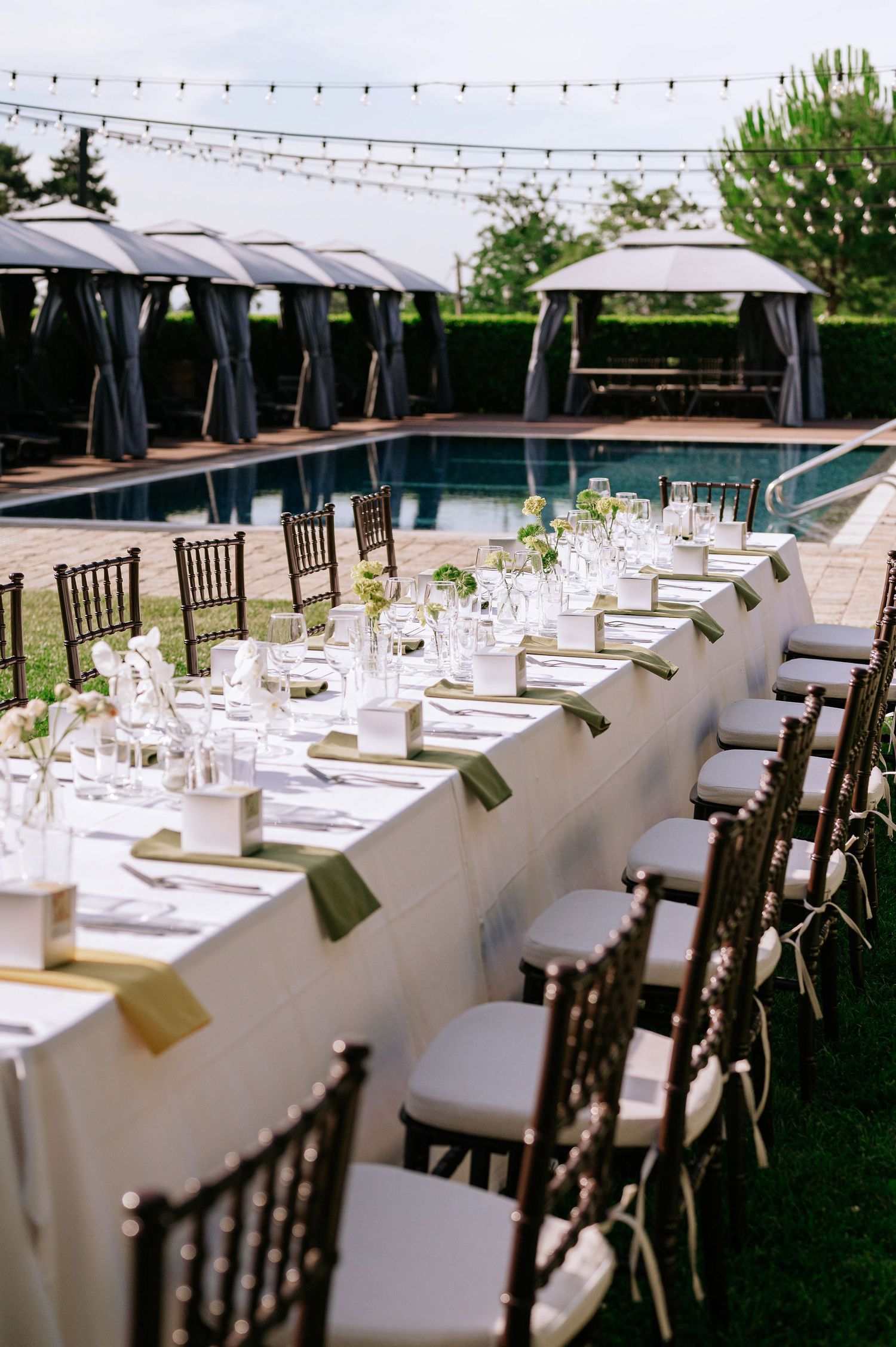 White-clothed dining tables with dark wooden chairs set up for an outdoor reception.