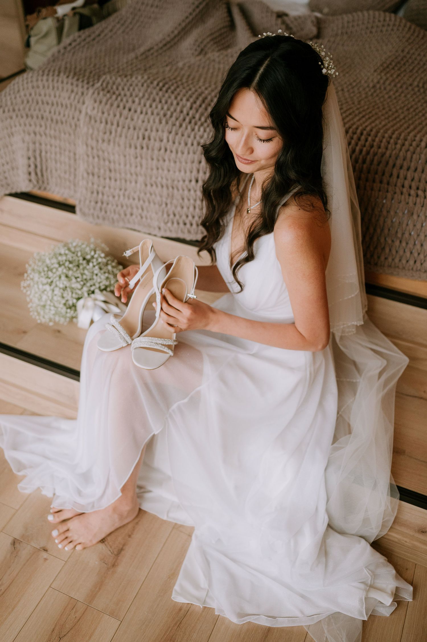 A white wedding dress flows gracefully across wooden flooring beside delicate floral arrangements.