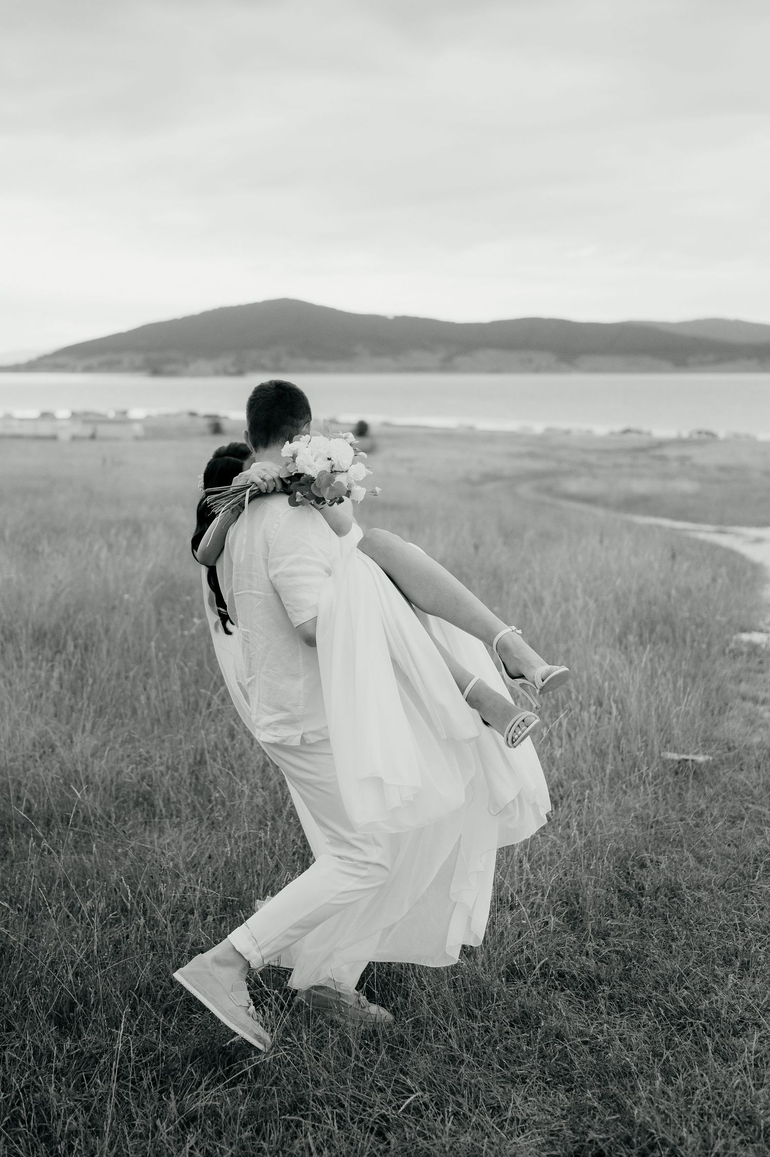Black and white photo of a wedding dance lift in a windswept coastal field.