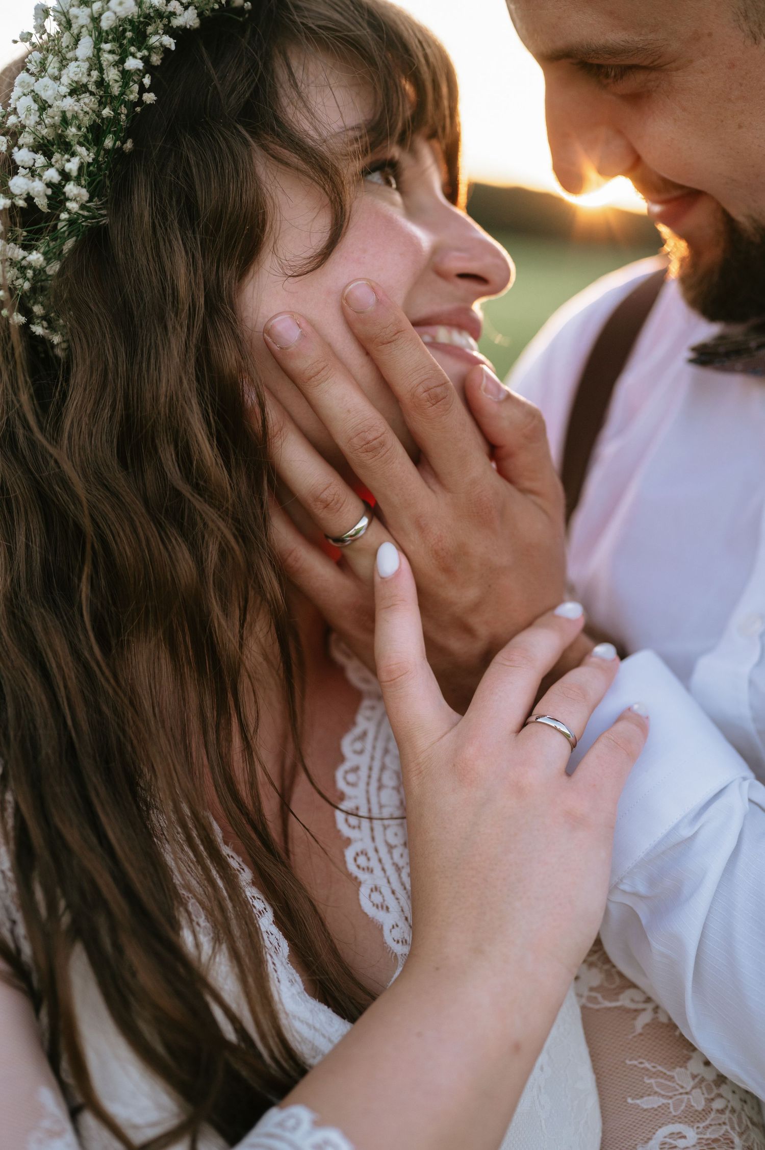 Close-up of tender moment between newlyweds showing wedding rings and floral crown.