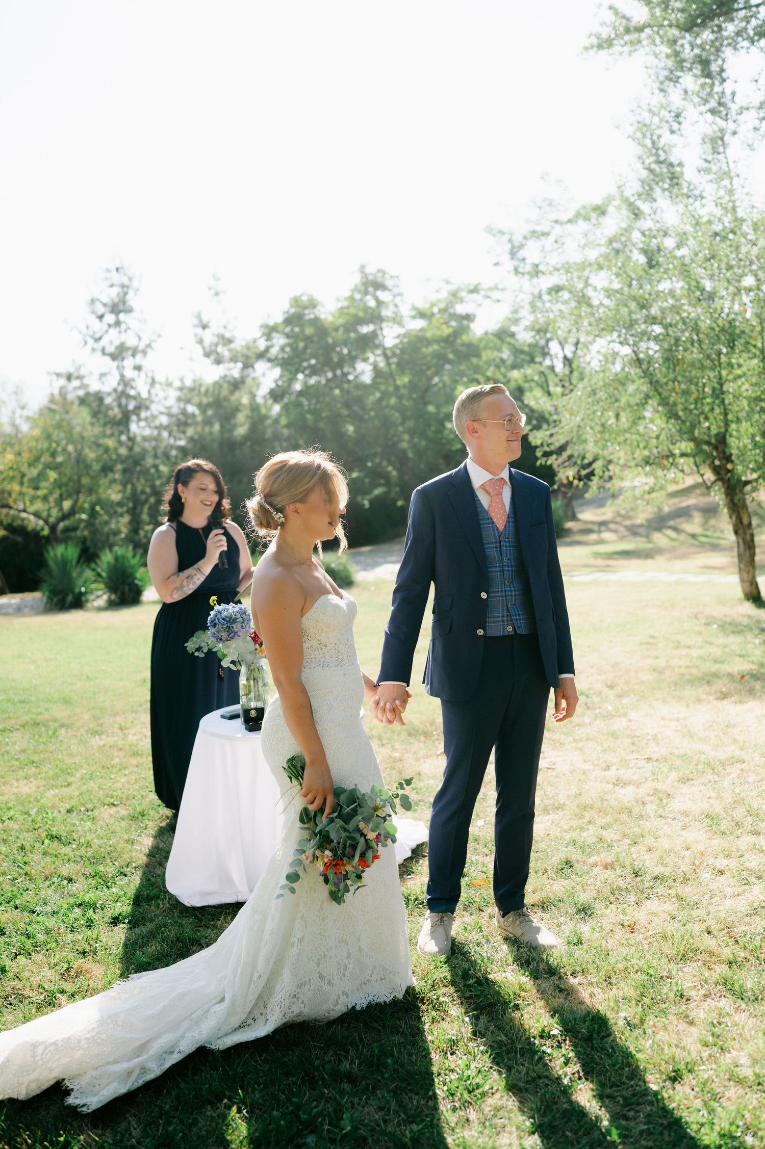 Wedding party members walk together across sunny field during photo session.
