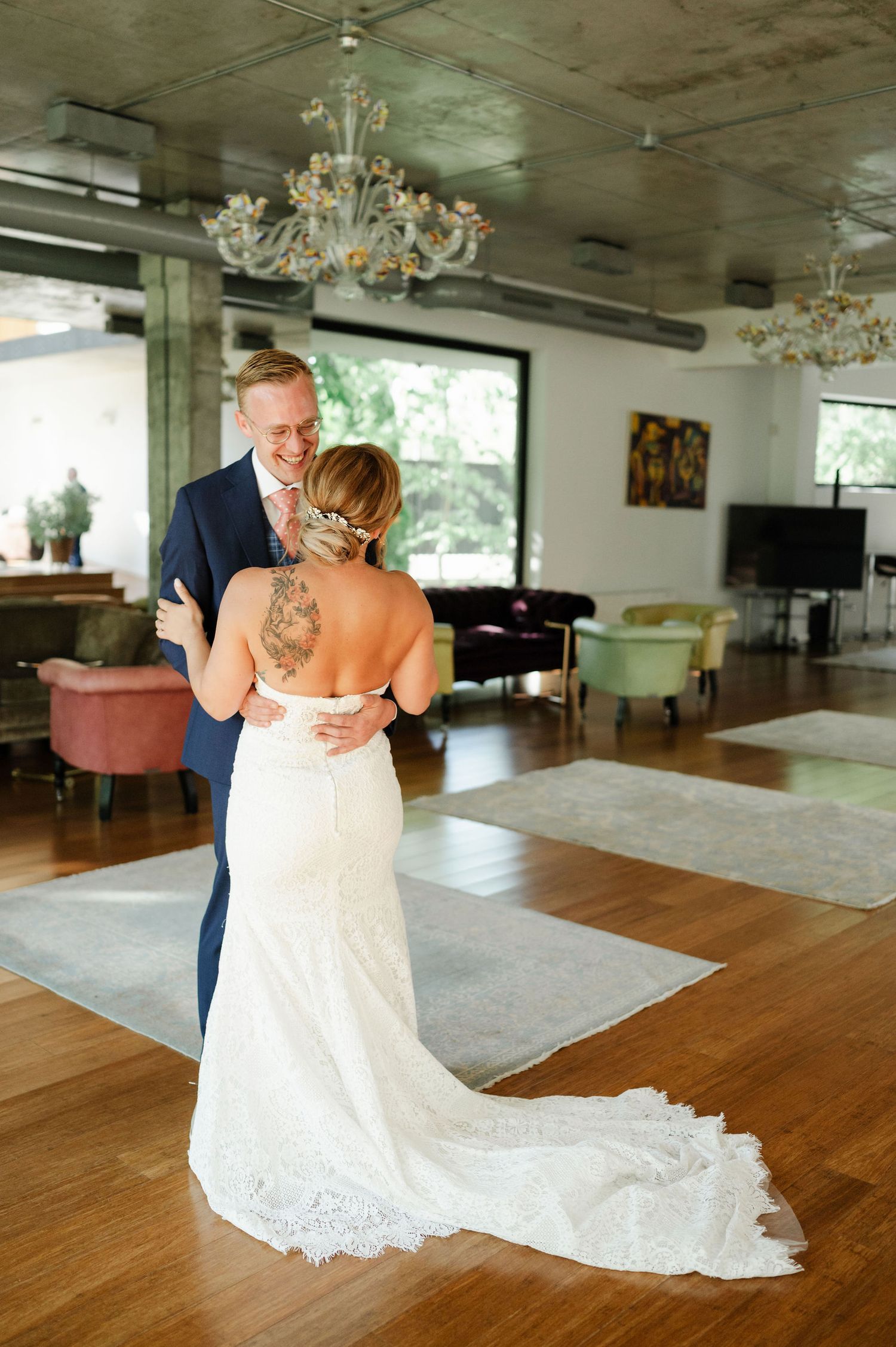 Couple in wedding attire dancing together in an elegant venue with hardwood floors and chandeliers.