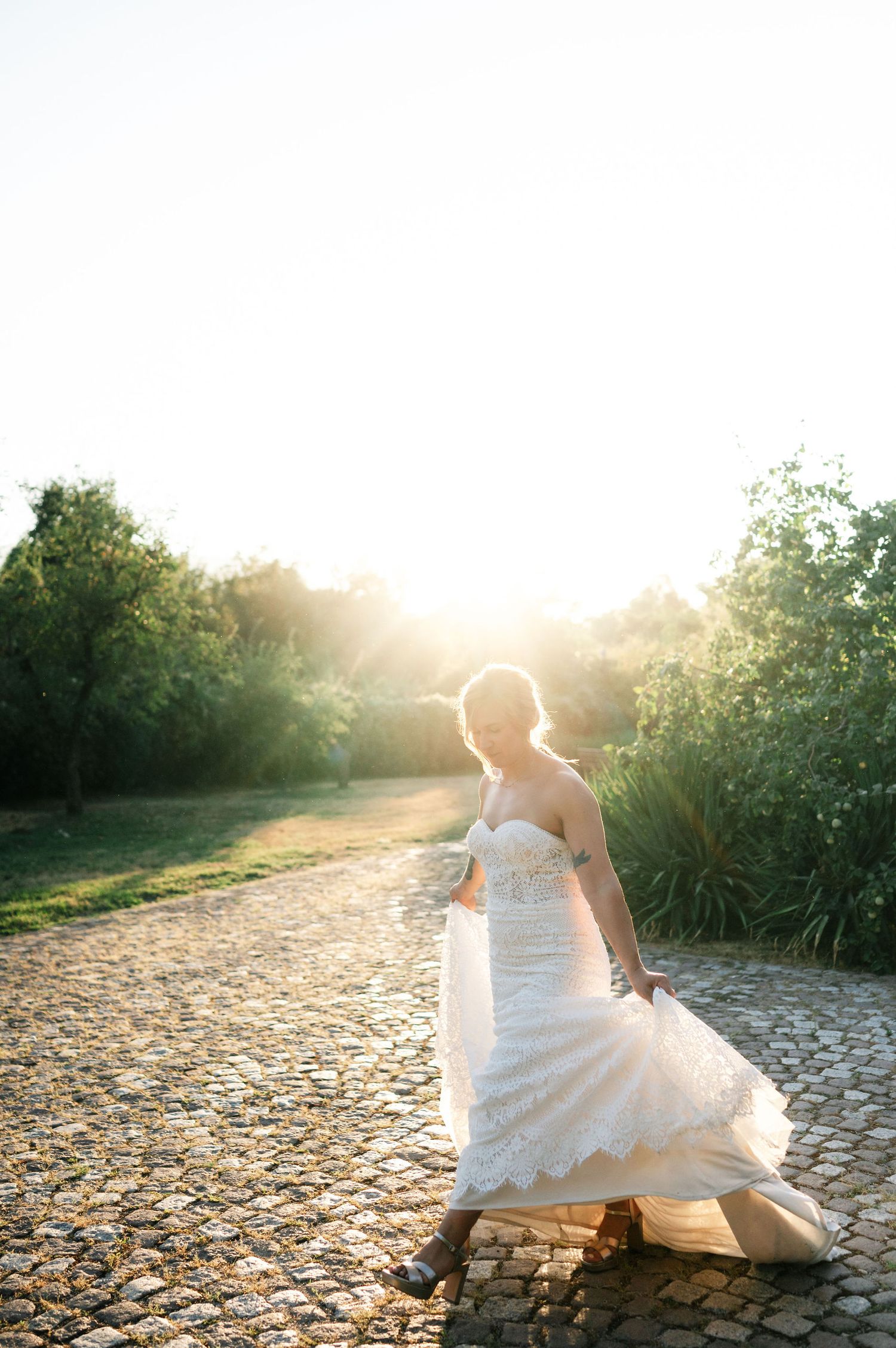 Dreamy wedding photo with white gown flowing over rustic stone ground at sunset.