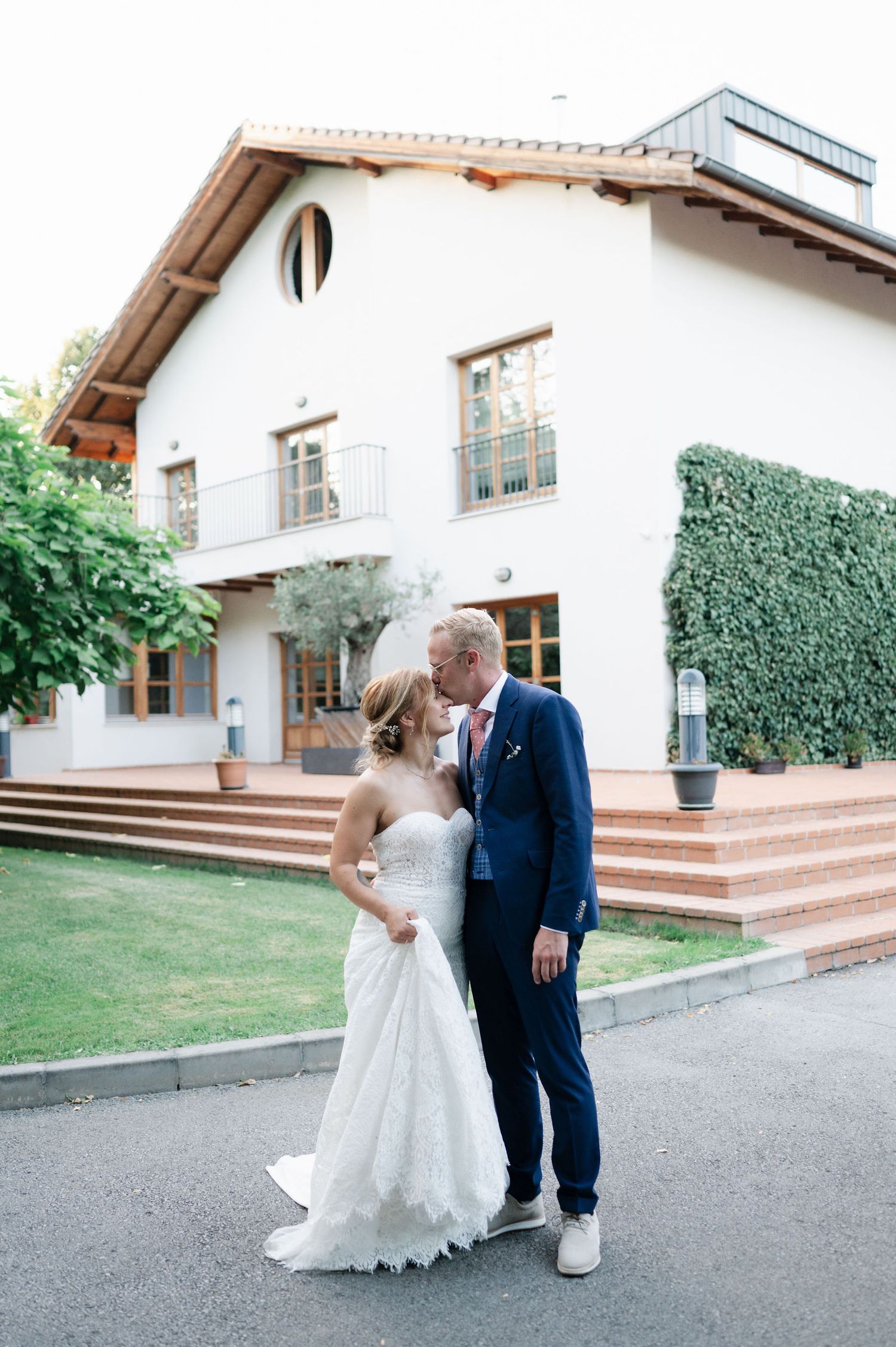 Newlyweds pose for romantic photos outside a Mediterranean-style house with ivy-covered walls.