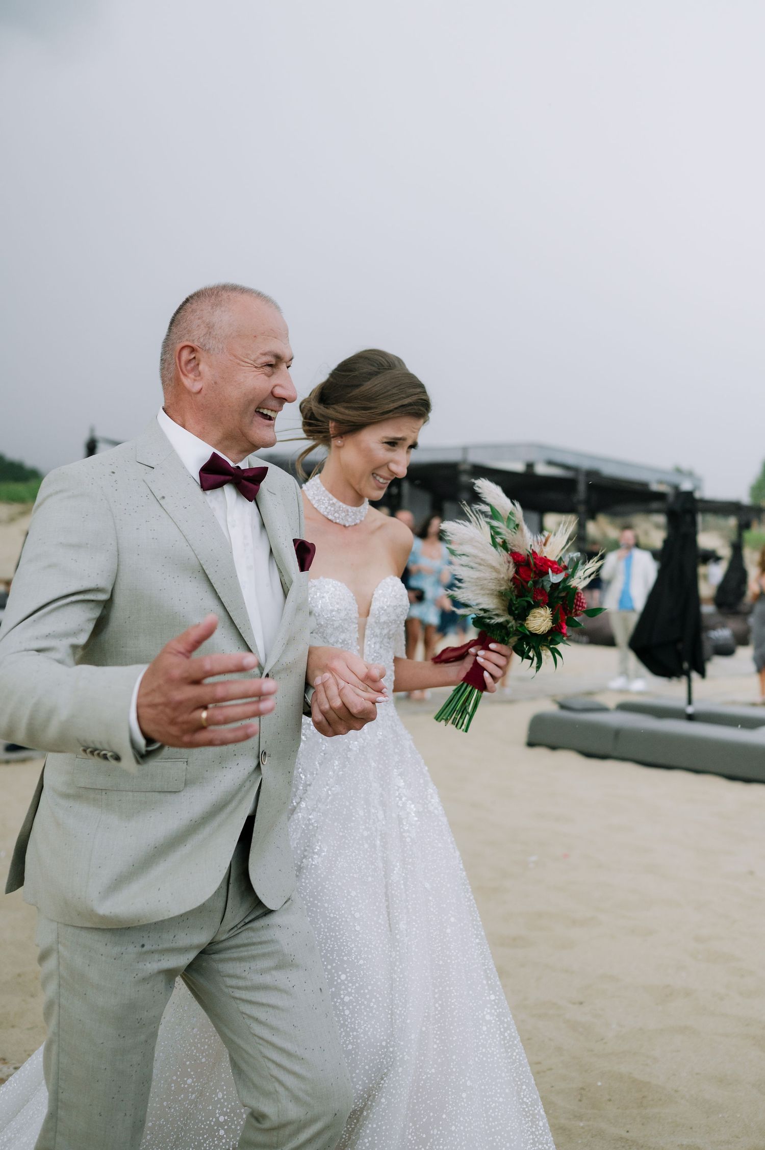 A couple shares a joyful moment while walking on a beach boardwalk in formal wedding attire.