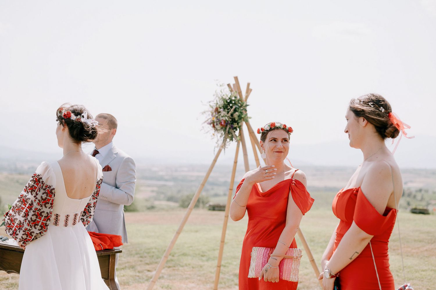 Wedding celebration on a hilltop with guests in red and white attire gathering near wooden decor.