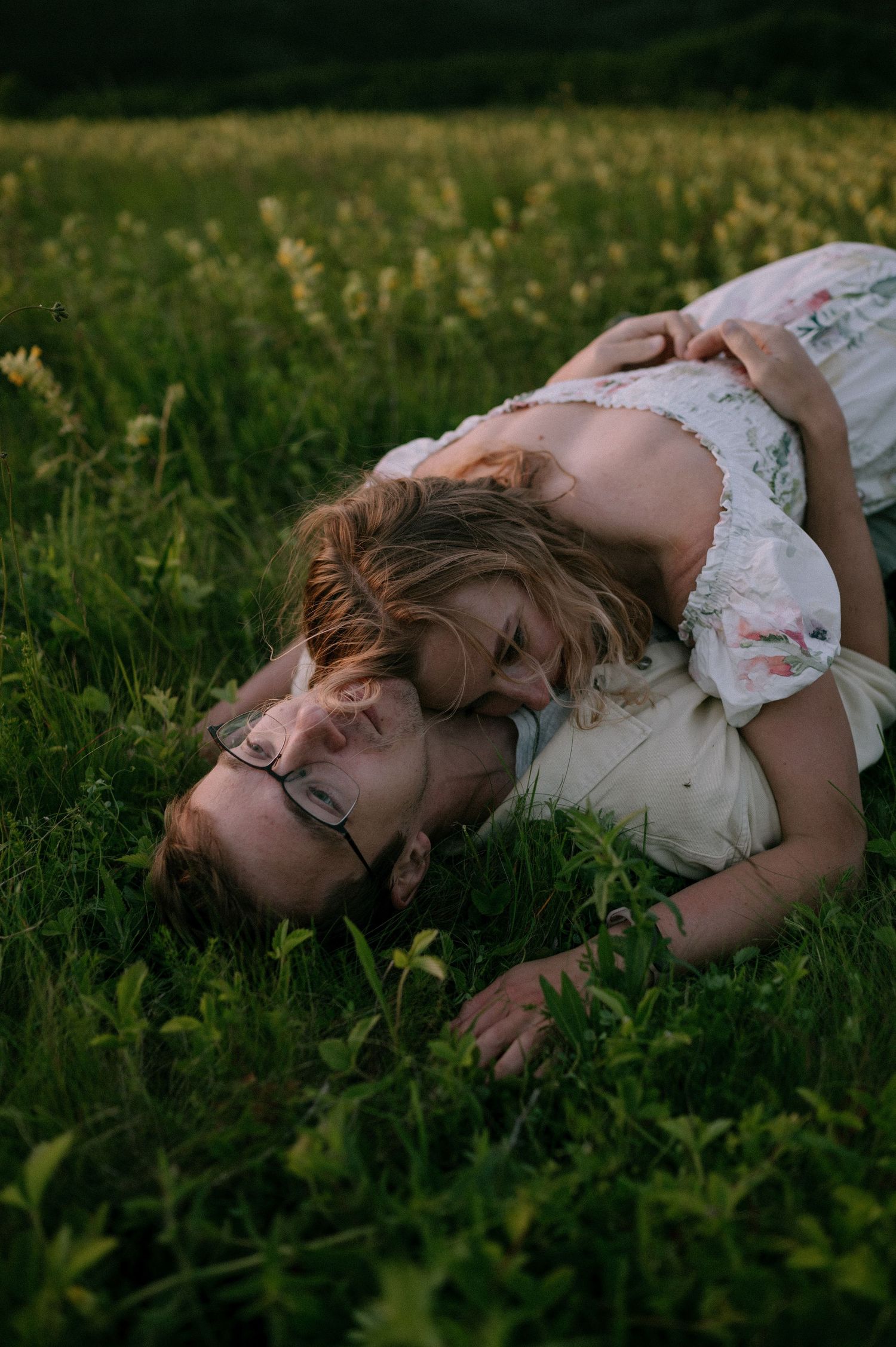 A person in a floral dress rests peacefully in a meadow during golden hour.