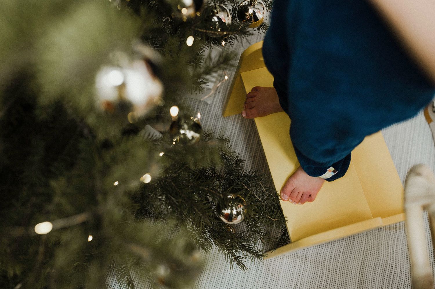 A close-up view of hands placing ornaments on a decorated Christmas tree with twinkling lights.