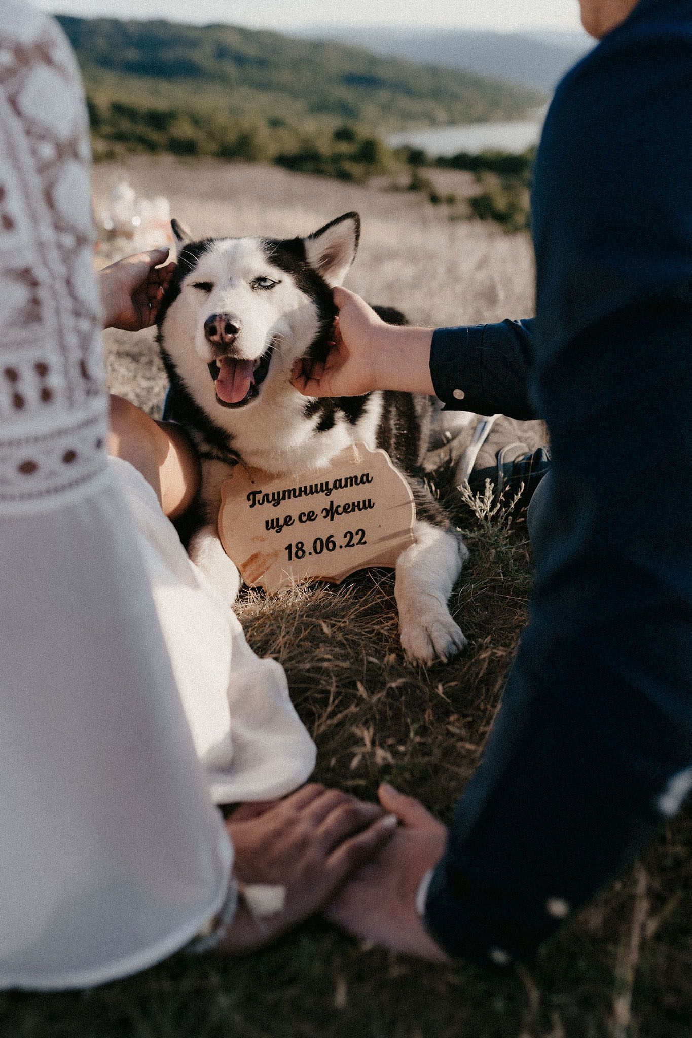 White husky dog with date inscription sitting between couple on rocky terrain.