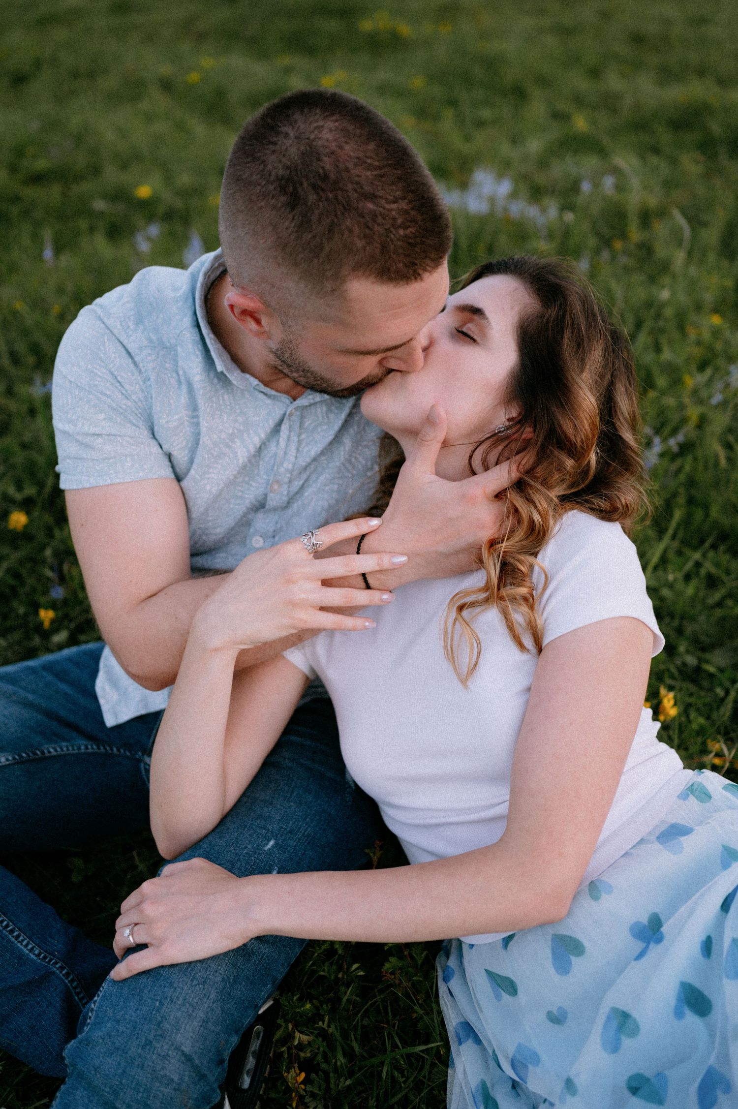 Couple embracing on grass with a light blue blanket in a sunny meadow.