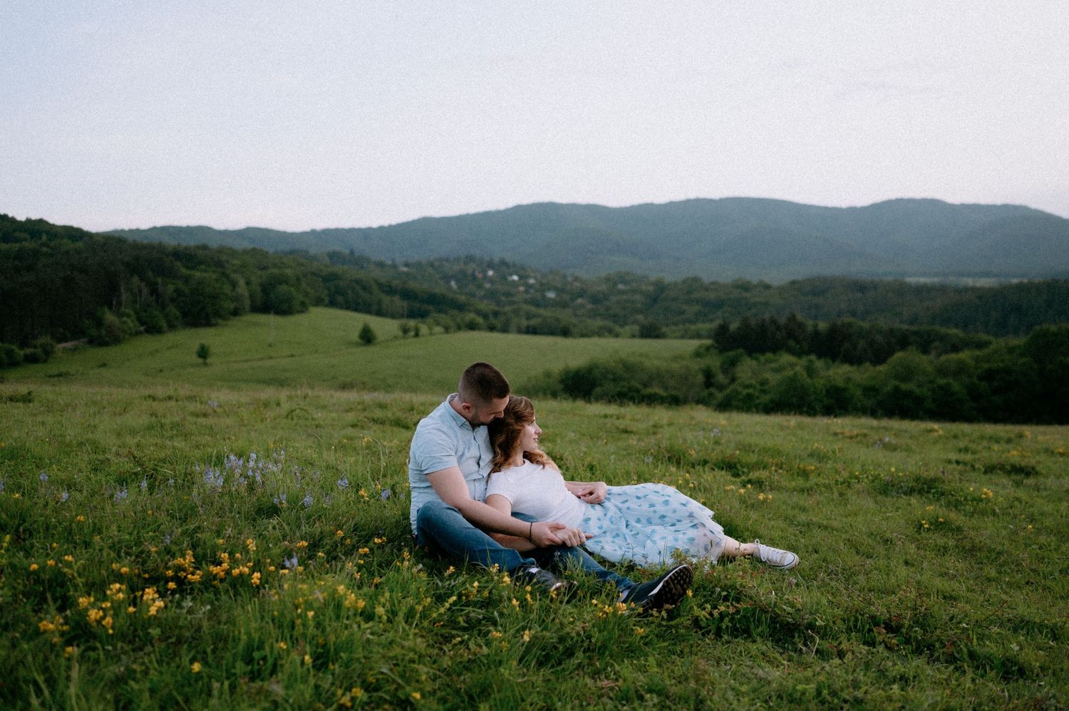 A couple relaxes together in a scenic mountain field with yellow wildflowers.