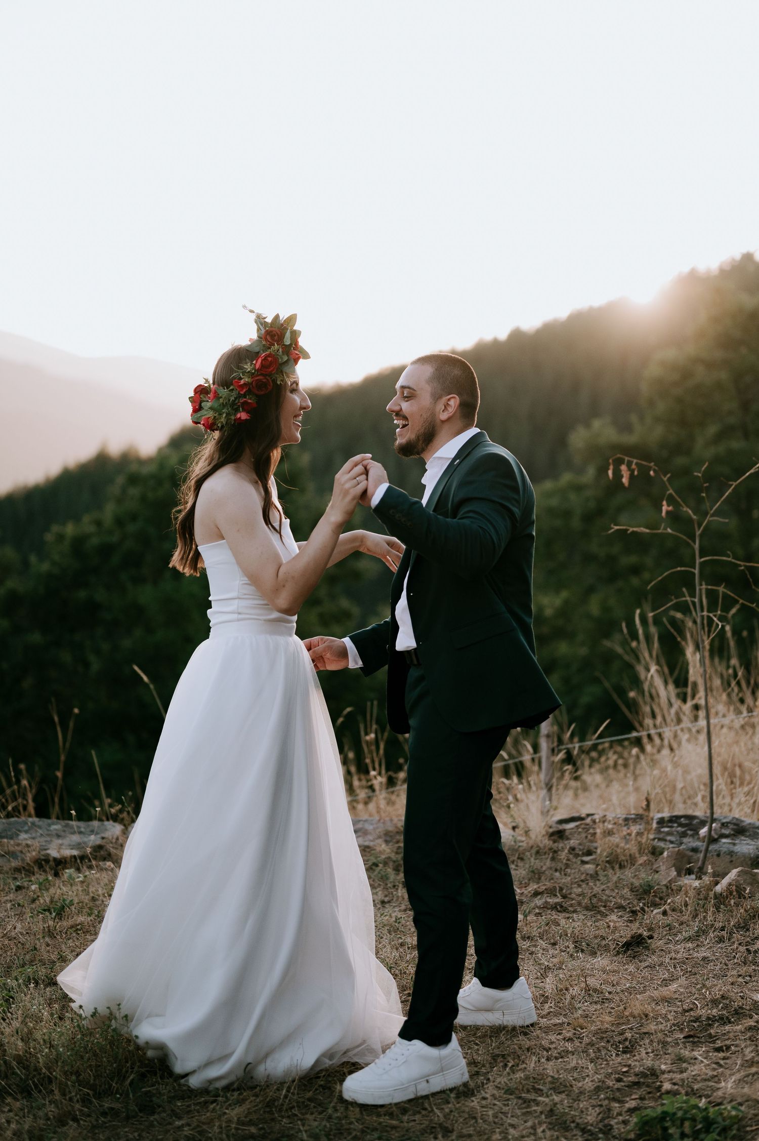 Couple in wedding attire dancing together on a hilltop at sunset.