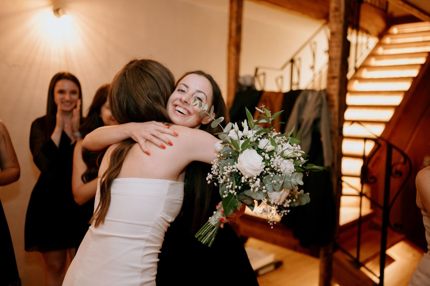 Wedding party celebrating with dancing and floral bouquets in rustic indoor venue.