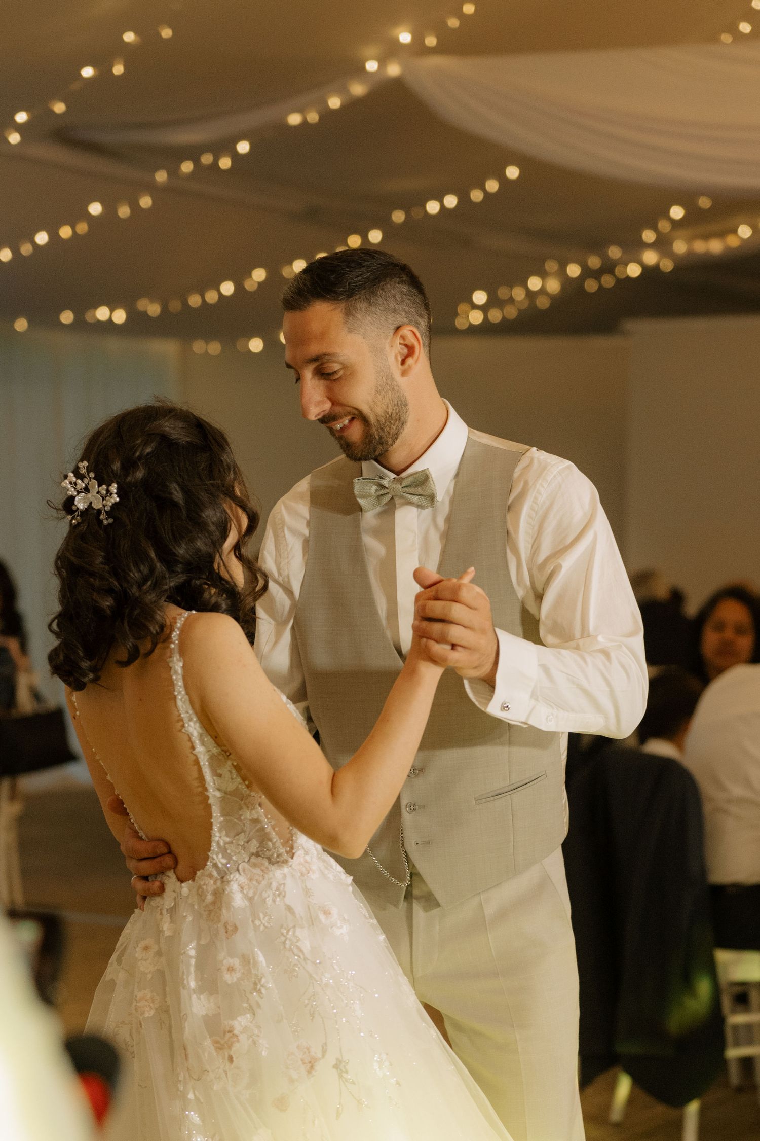 Bride and groom share their first dance under twinkling fairy lights at elegant wedding reception.