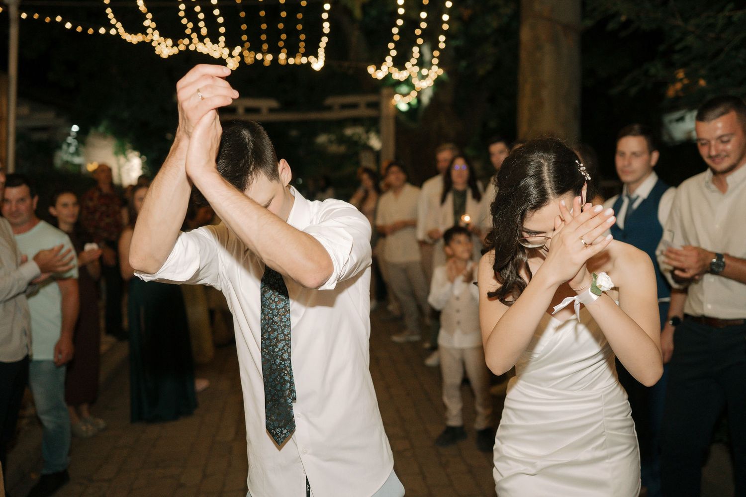 Couples dancing together at a wedding reception under twinkling string lights in a romantic evening celebration.
