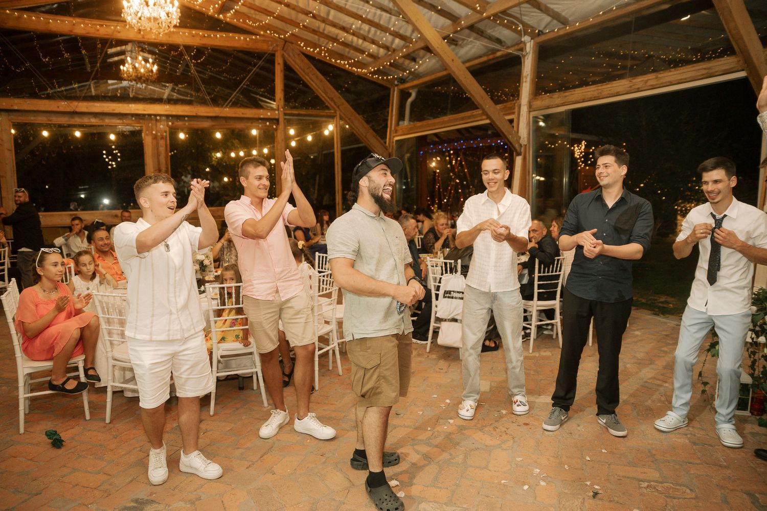 Wedding guests perform a synchronized dance routine in a rustic barn venue with twinkling lights overhead.