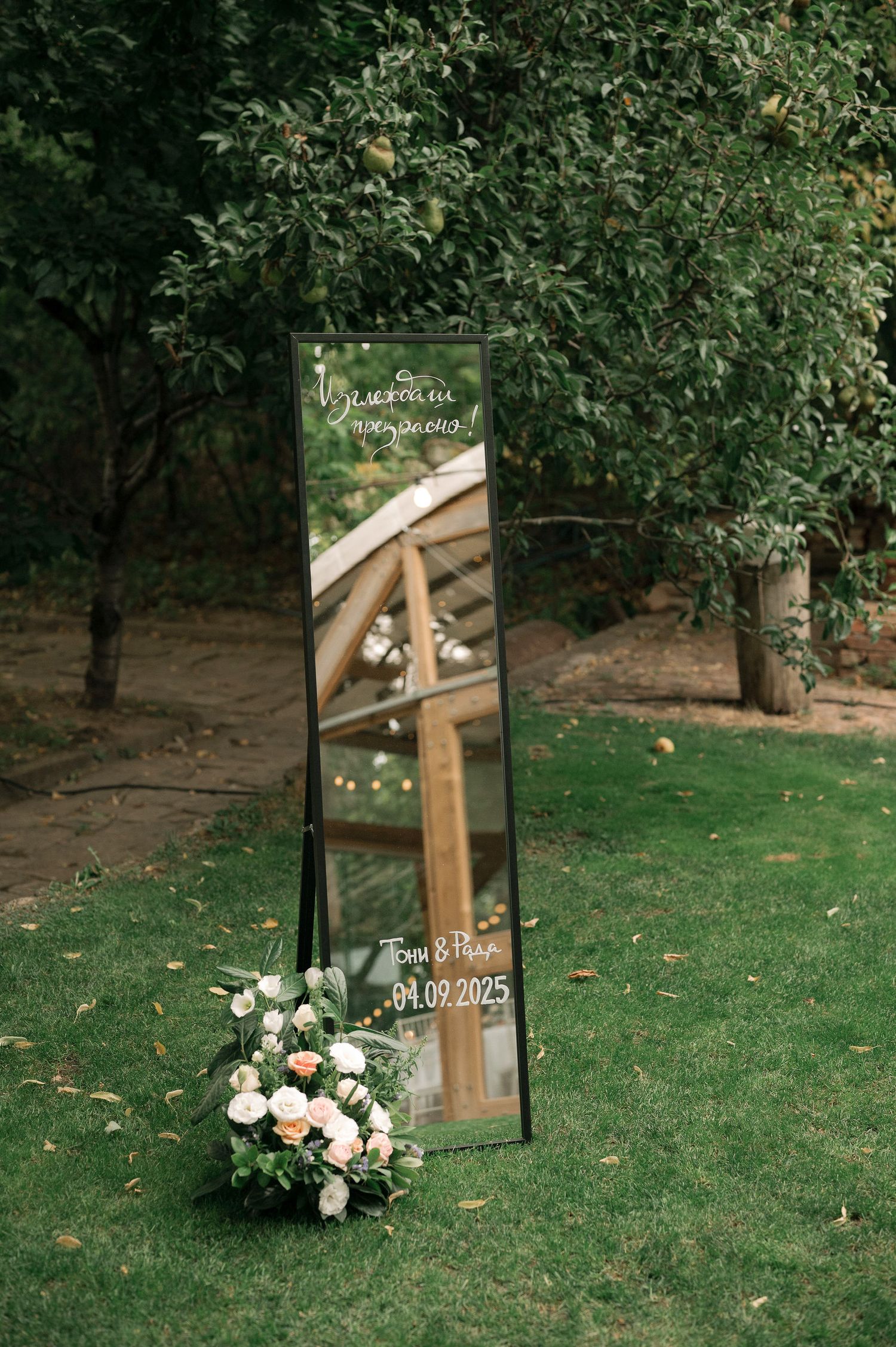 Rustic wooden wedding welcome sign with floral arrangements displayed on green grass in an outdoor garden setting.