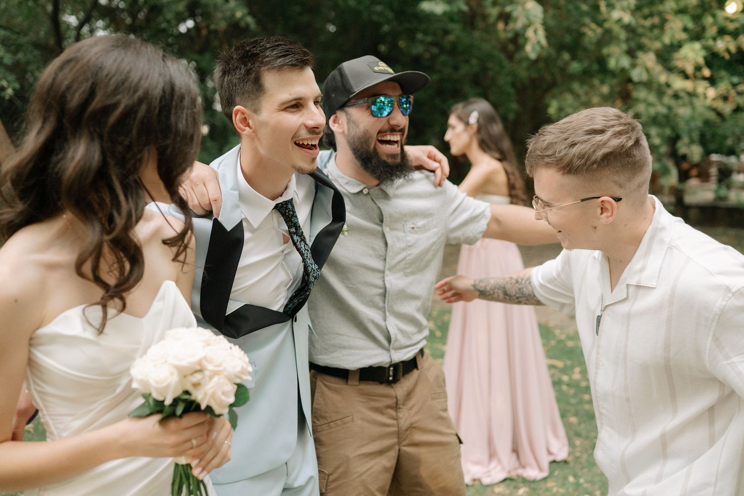 A wedding party dances and celebrates together in an outdoor garden setting with soft pink and white decor.
