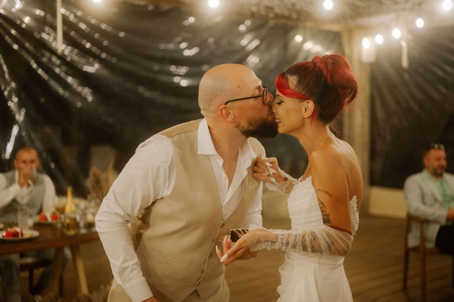 A romantic wedding reception under string lights with couples dancing and embracing on the dance floor.