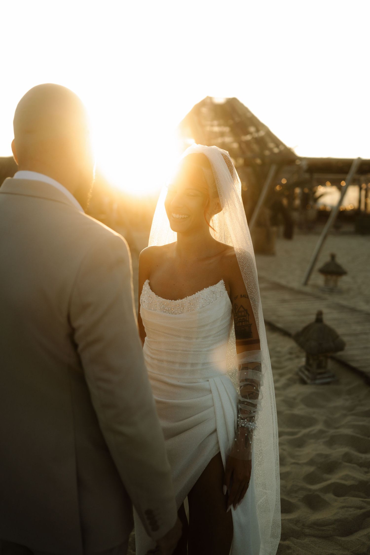 A romantic silhouette of a couple embracing on a sandy beach at sunset with golden sunlight streaming behind them.