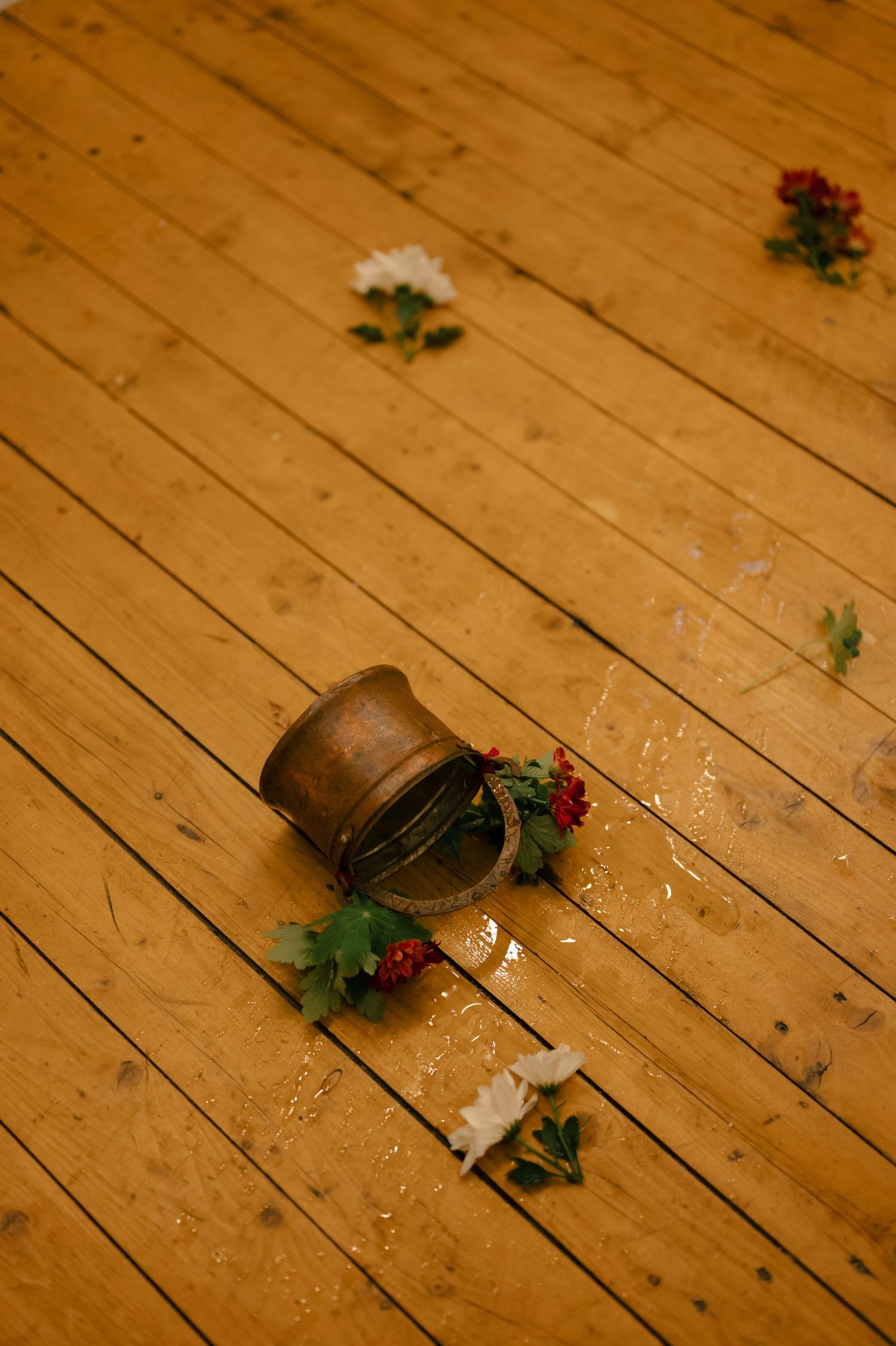 A rustic wooden floor with scattered flowers and a vintage metal pot creating a romantic wedding detail.
