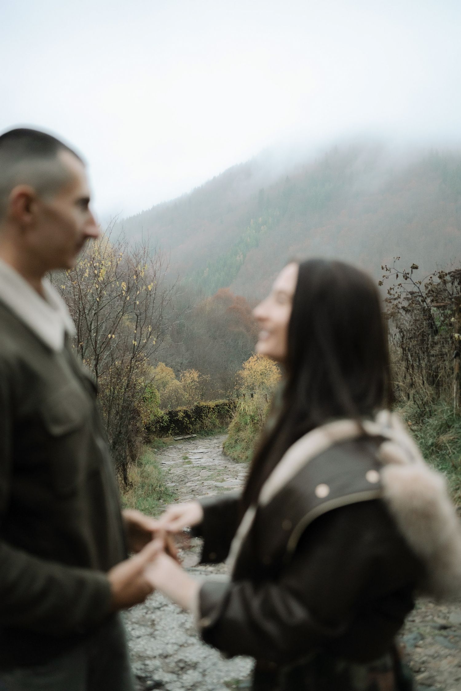 A couple shares an intimate moment on a misty mountain trail during what appears to be an engagement or proposal.