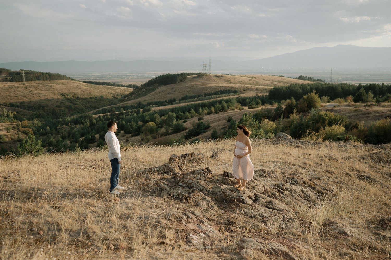 A couple walks together through scenic rolling hills and grasslands during a golden sunset in Montana.