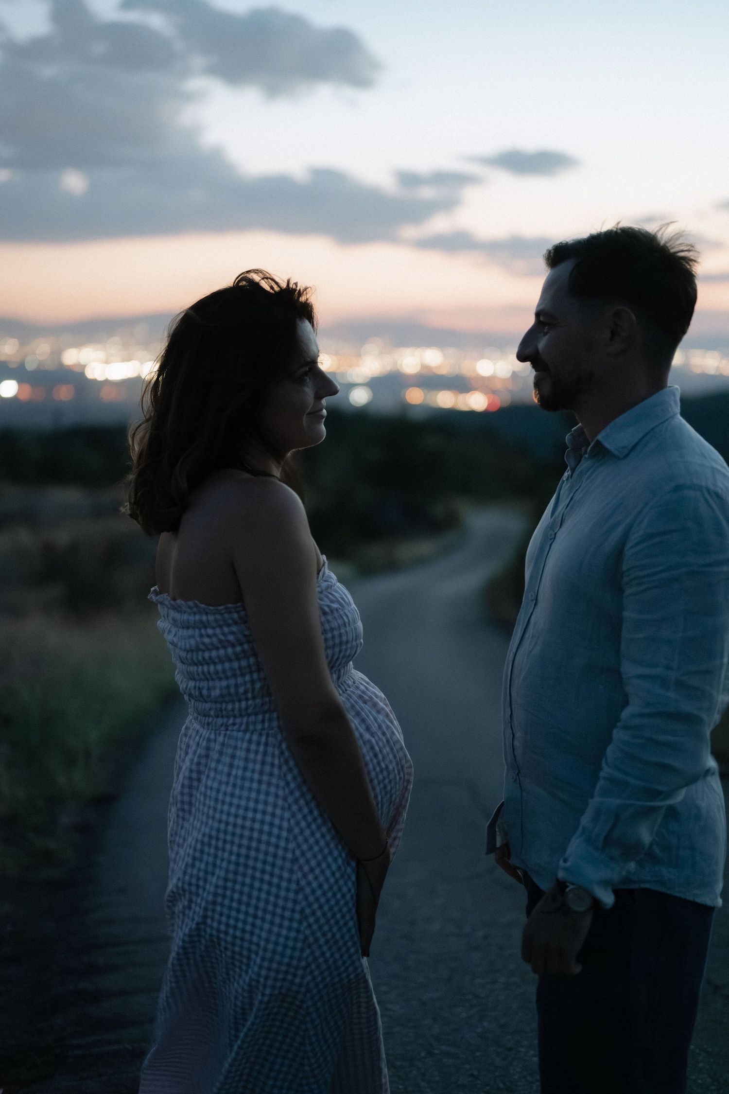A couple in silhouette shares a romantic moment at sunset against a cloudy sky.