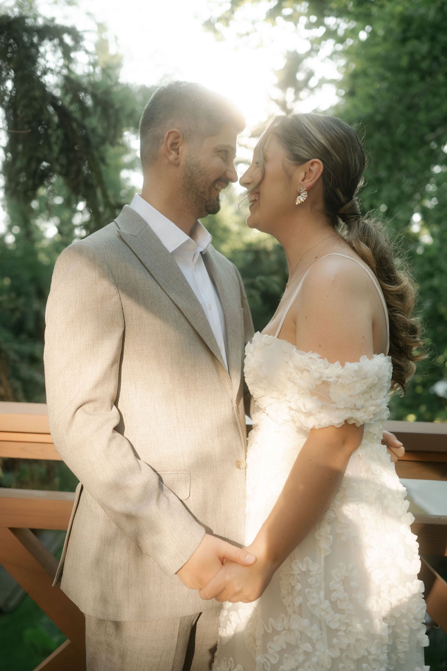 A romantic wedding moment captured outdoors with the couple in a beige suit and white off-shoulder gown.